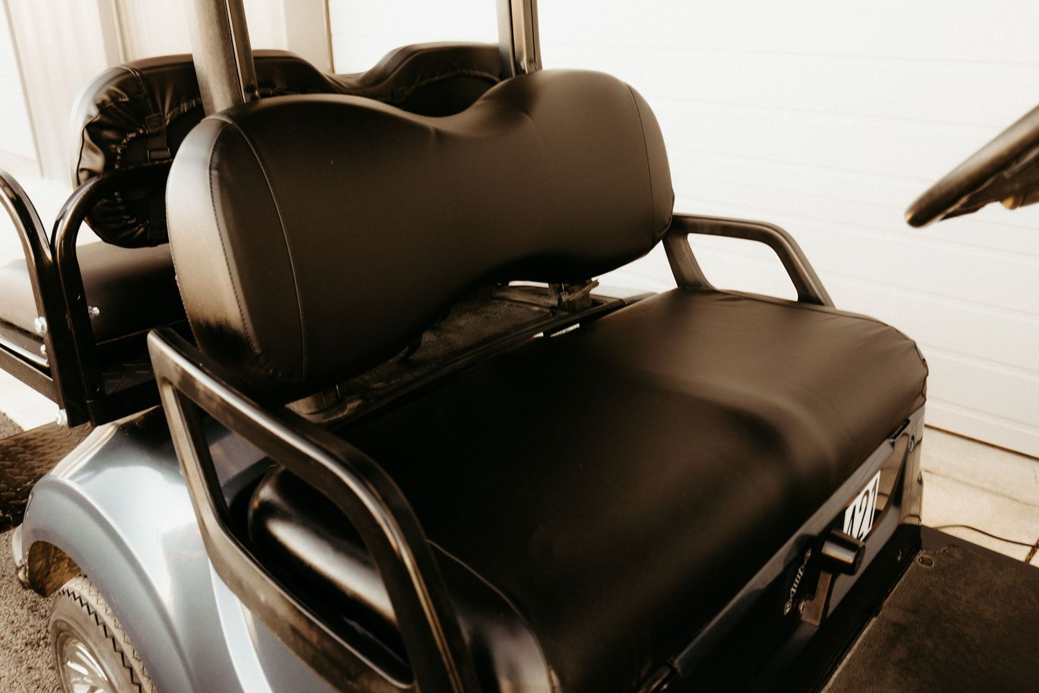 Black leather seat cushions and armrest on a golf cart shown in sepia-toned close up view.