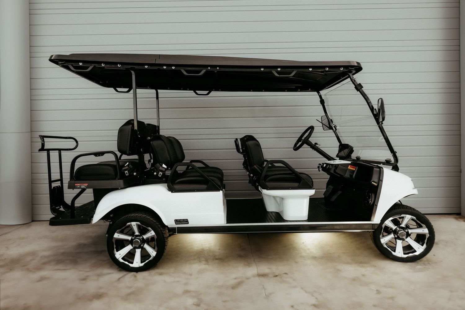 A white luxury golf cart with custom wheels and extended seating parked in a garage space.