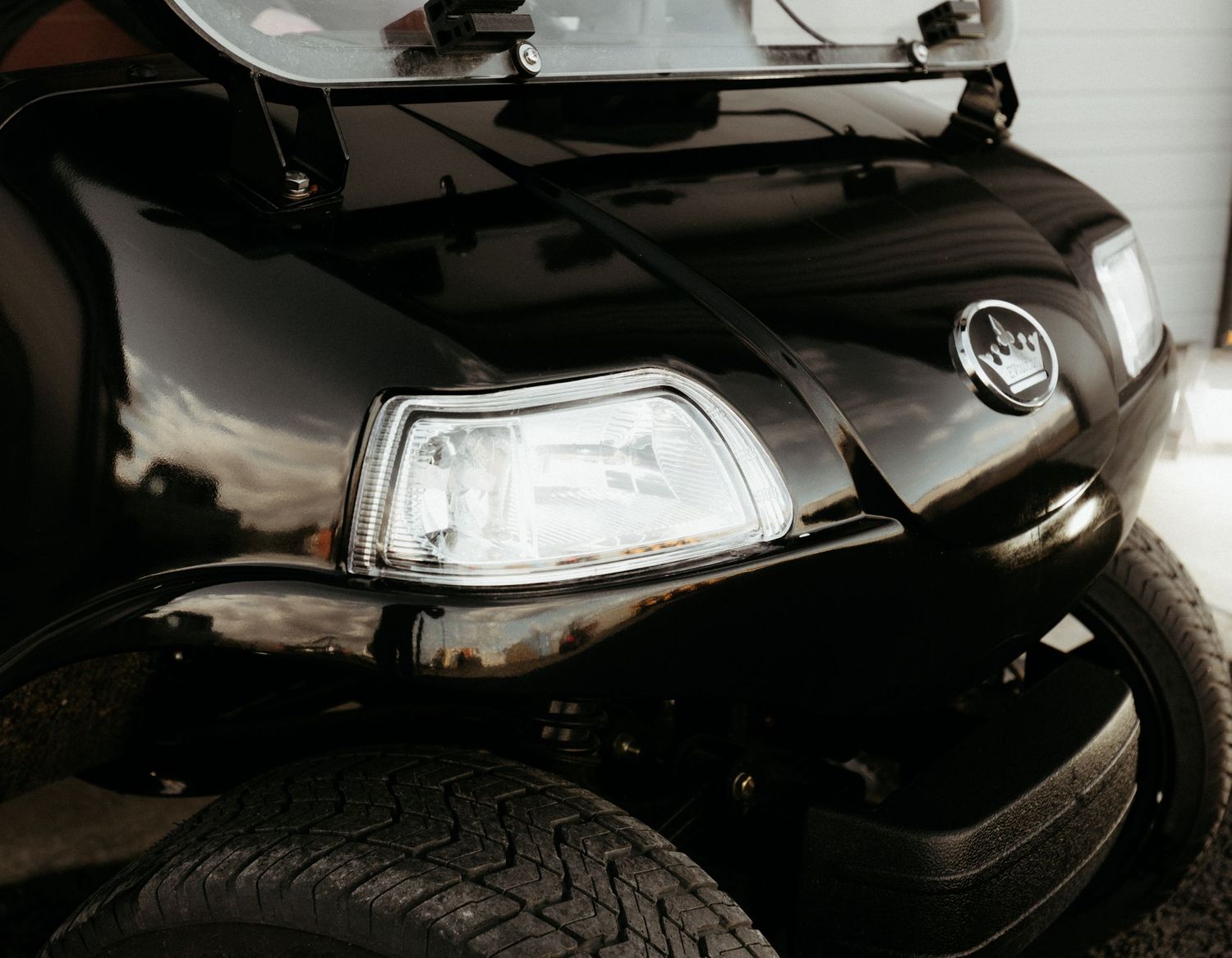 Close-up photo of a black car's damaged headlight and front bumper showing collision impact damage.