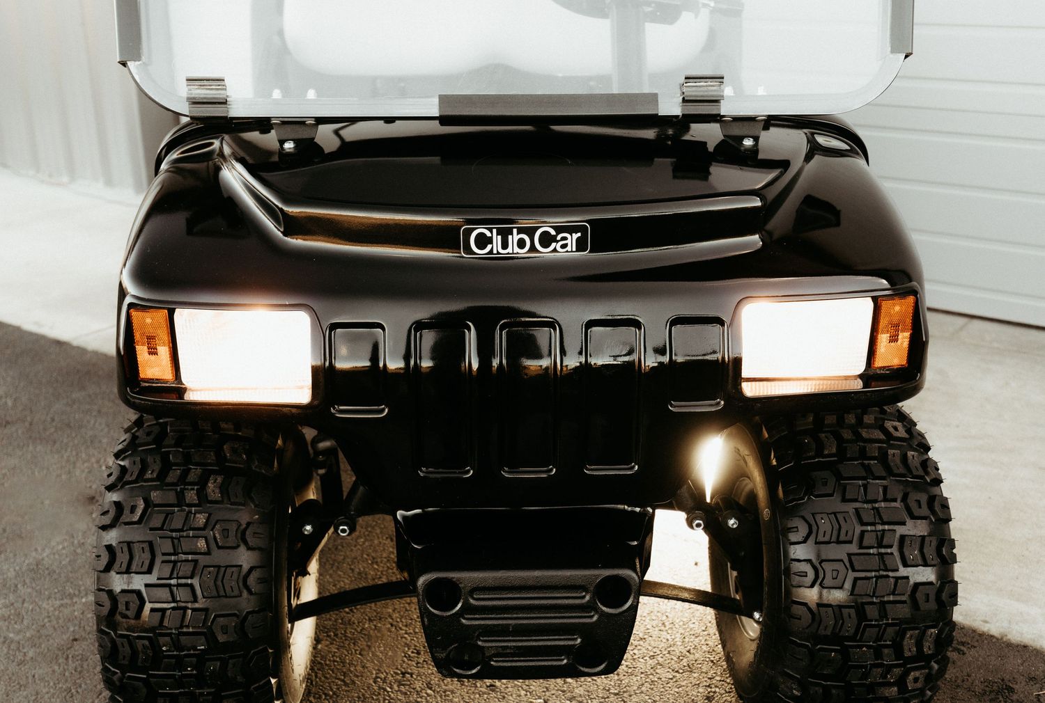 Close up view of black Club Car golf cart front end showing headlights and rugged all-terrain tires.
