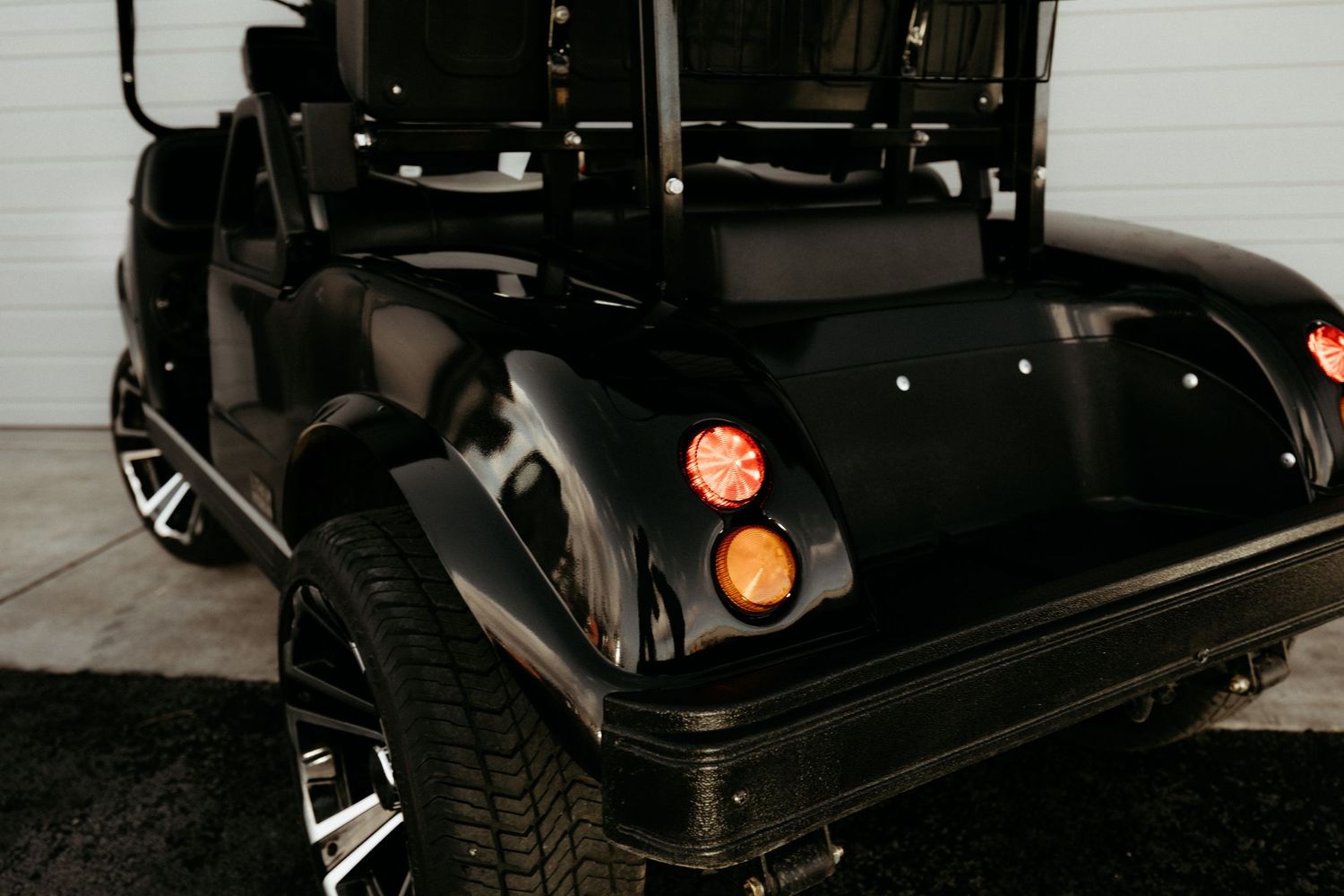 Close-up view of a black golf cart's front wheel and headlight details showing custom rims and styling.