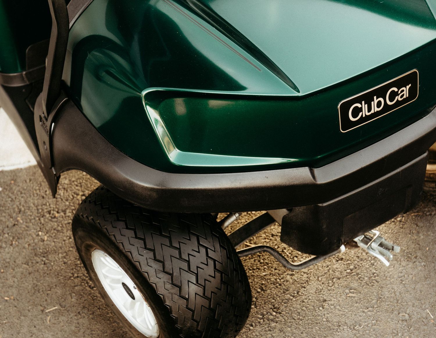 Close-up view of a green Club Car golf cart wheel and front bumper detail showing the rugged tire tread pattern.