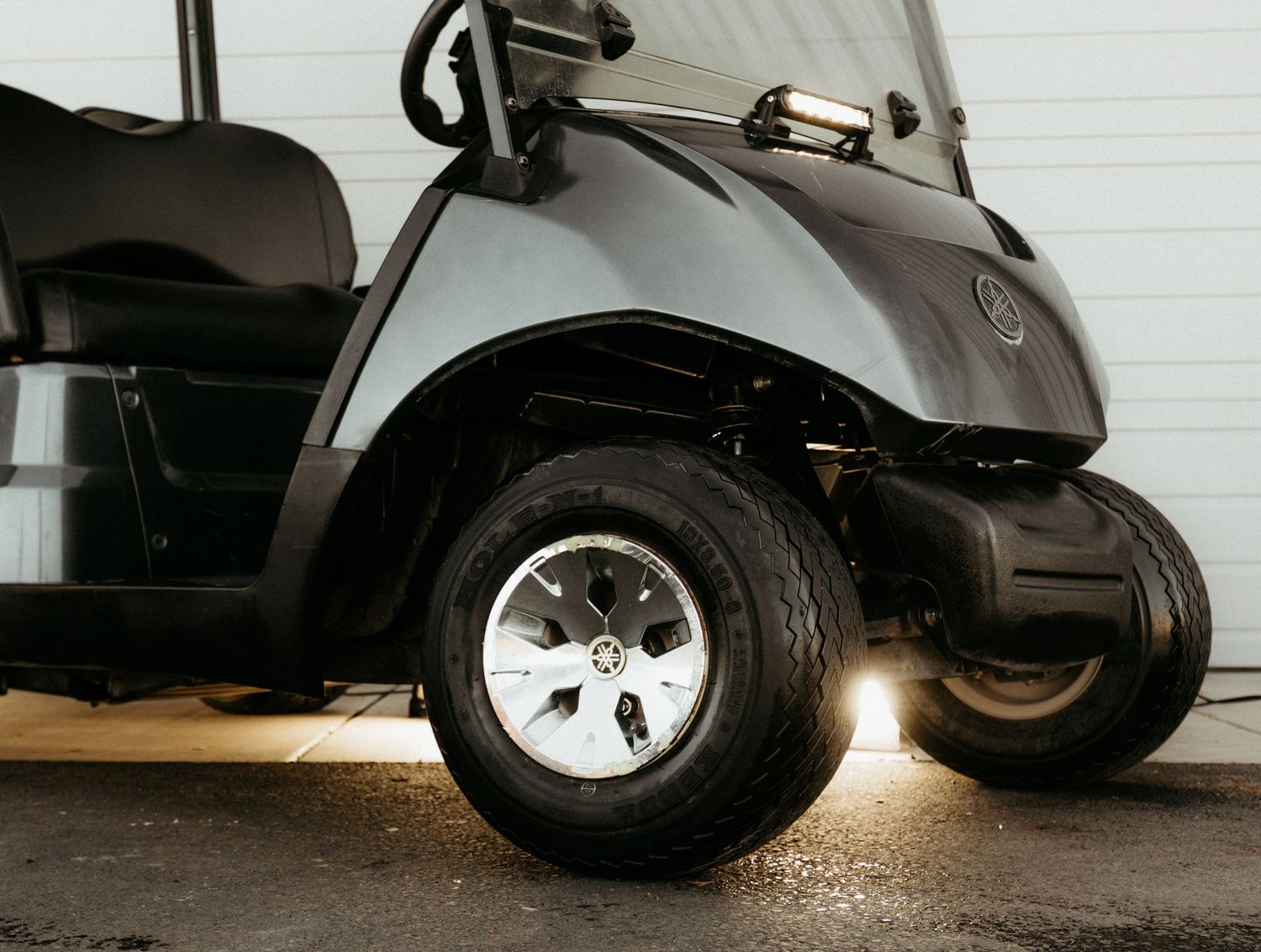 Close-up view of a golf cart wheel and tire on white painted pavement with dramatic shadowing.
