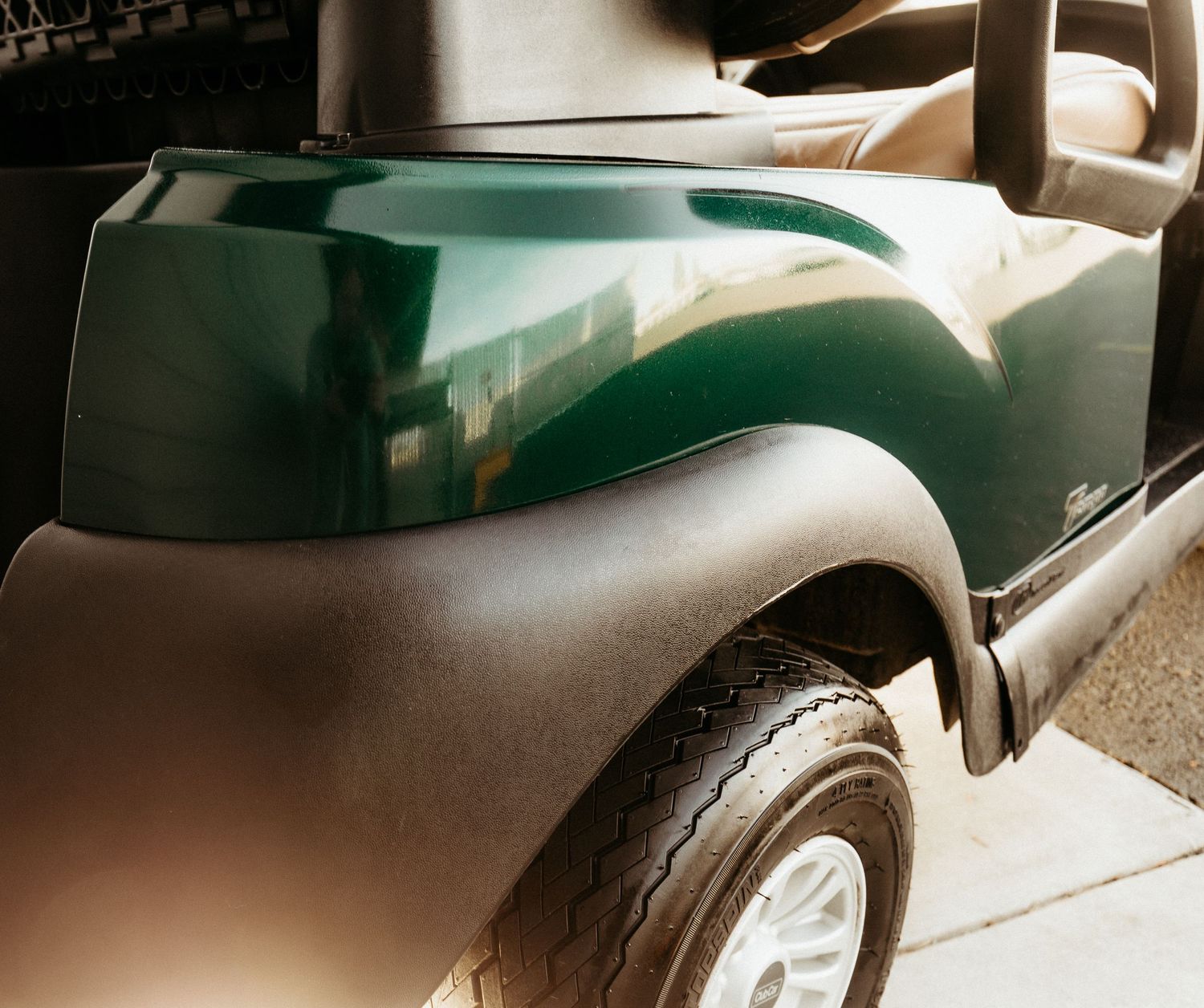 Close-up view of a dark green and gray golf cart fender and wheel in natural lighting.