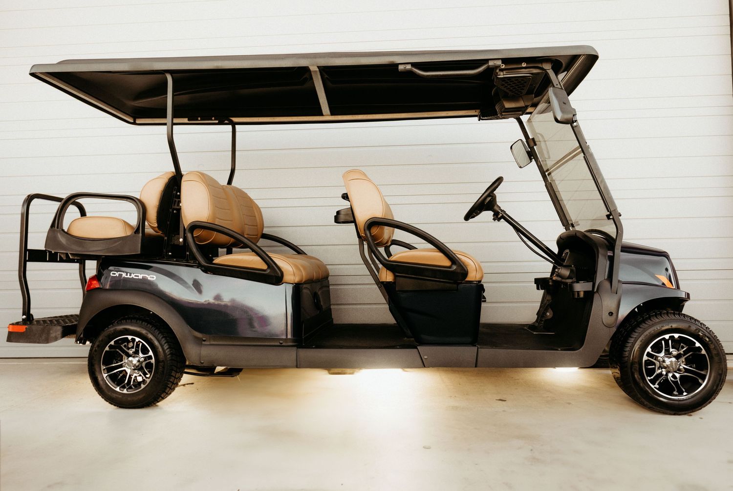 Stretched golf cart with dark gray exterior and tan seats parked in a bright indoor space.