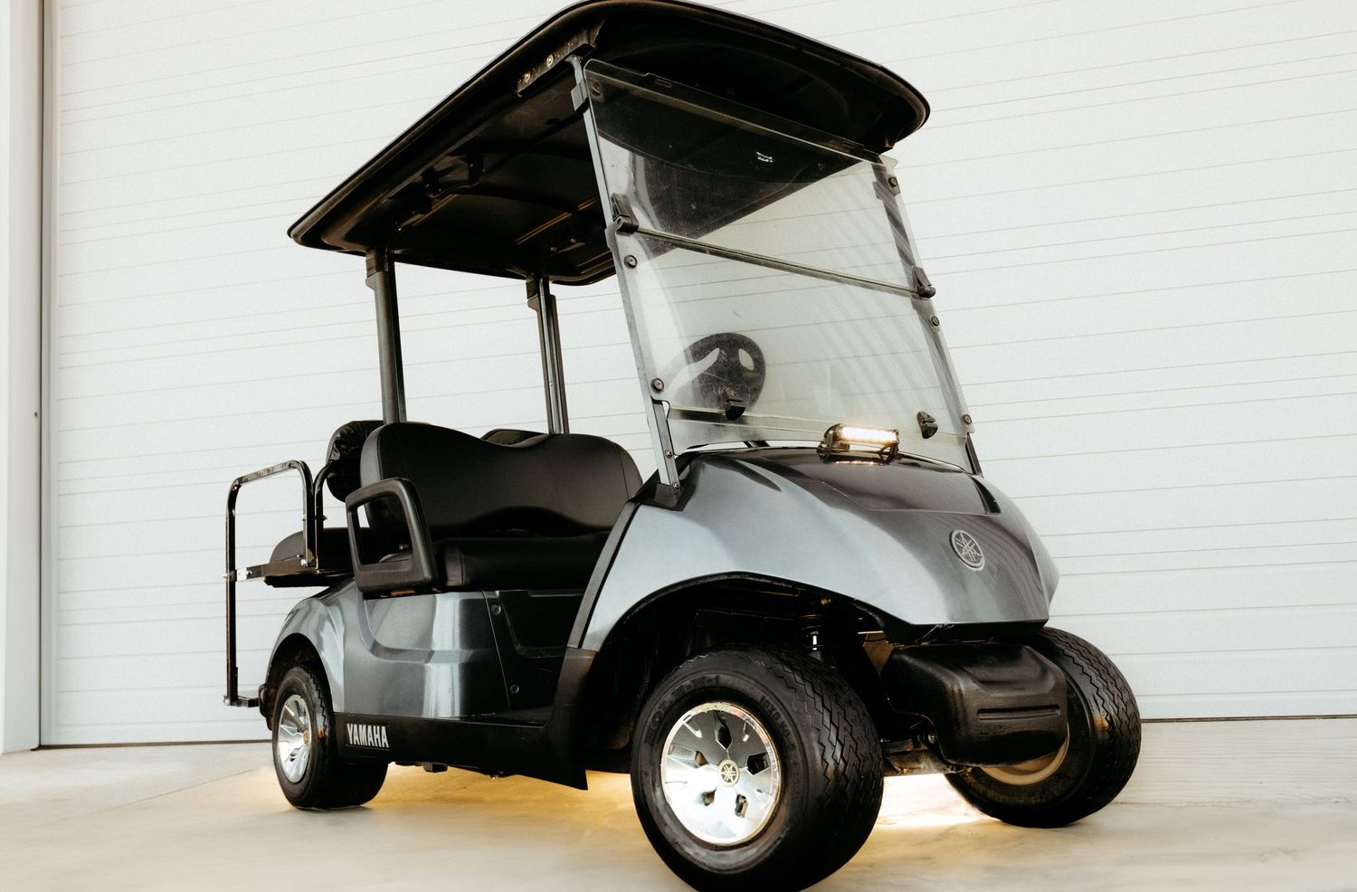 A silver and black golf cart with custom wheels parked indoors against a white wall.