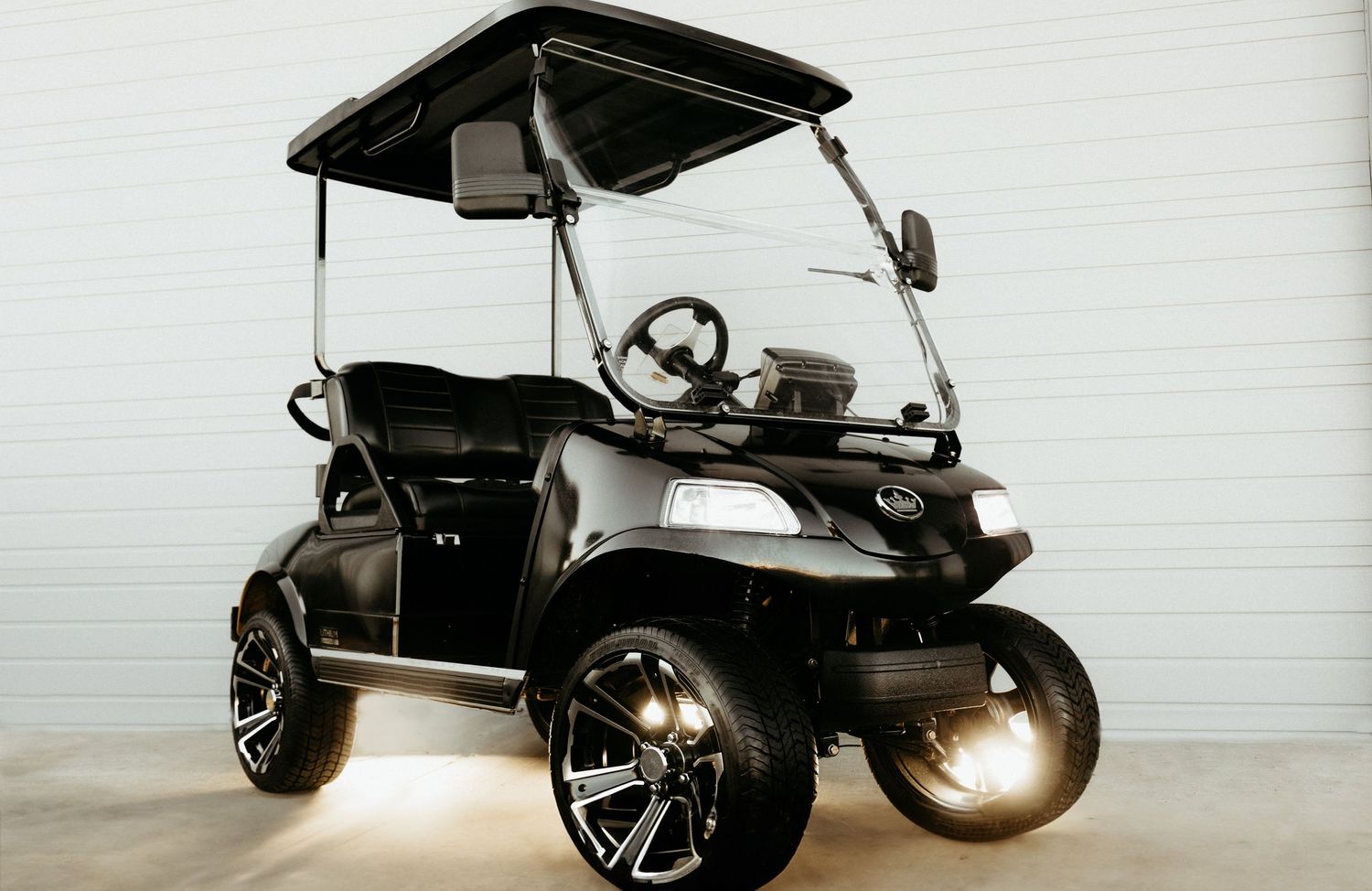 Custom black golf cart with oversized chrome wheels and LED underbody lighting against white background.
