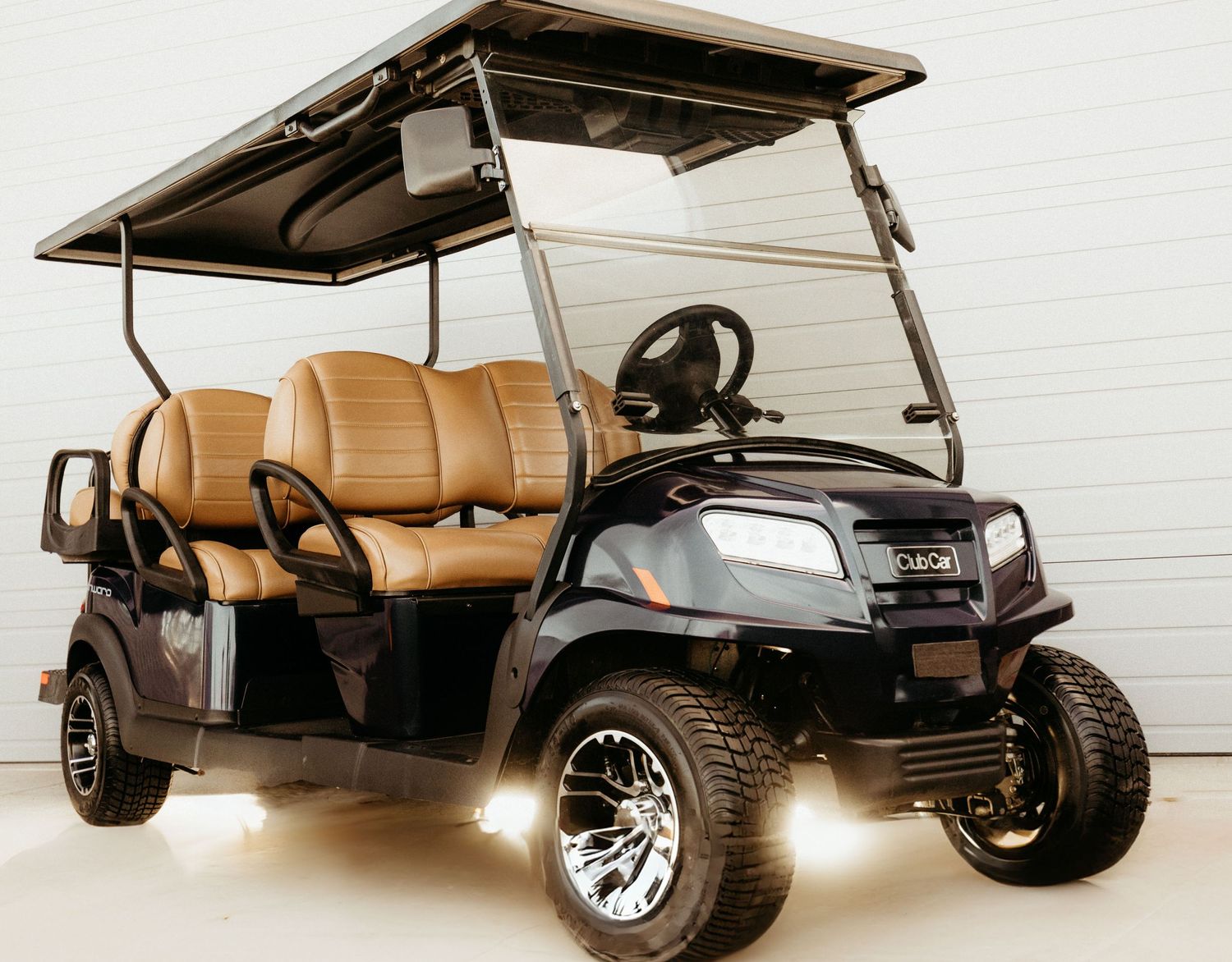 Custom black golf cart with tan leather seats, chrome wheels and extended seating capacity parked indoors.