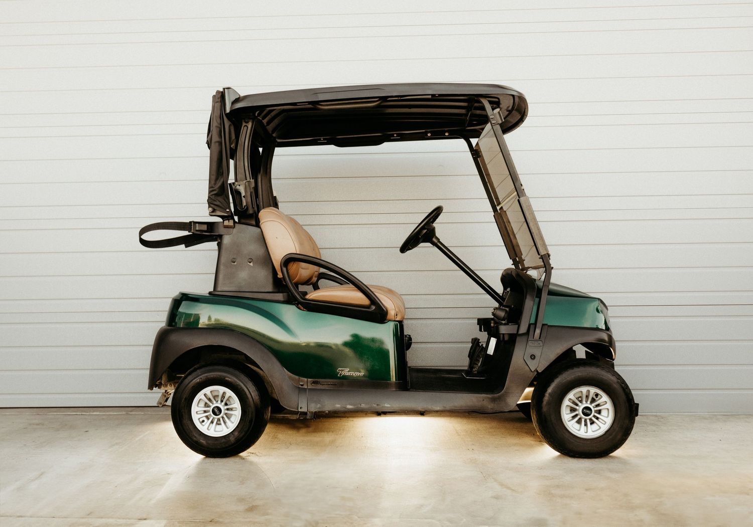 A green golf cart with tan seats parked against a white wall in a garage setting.