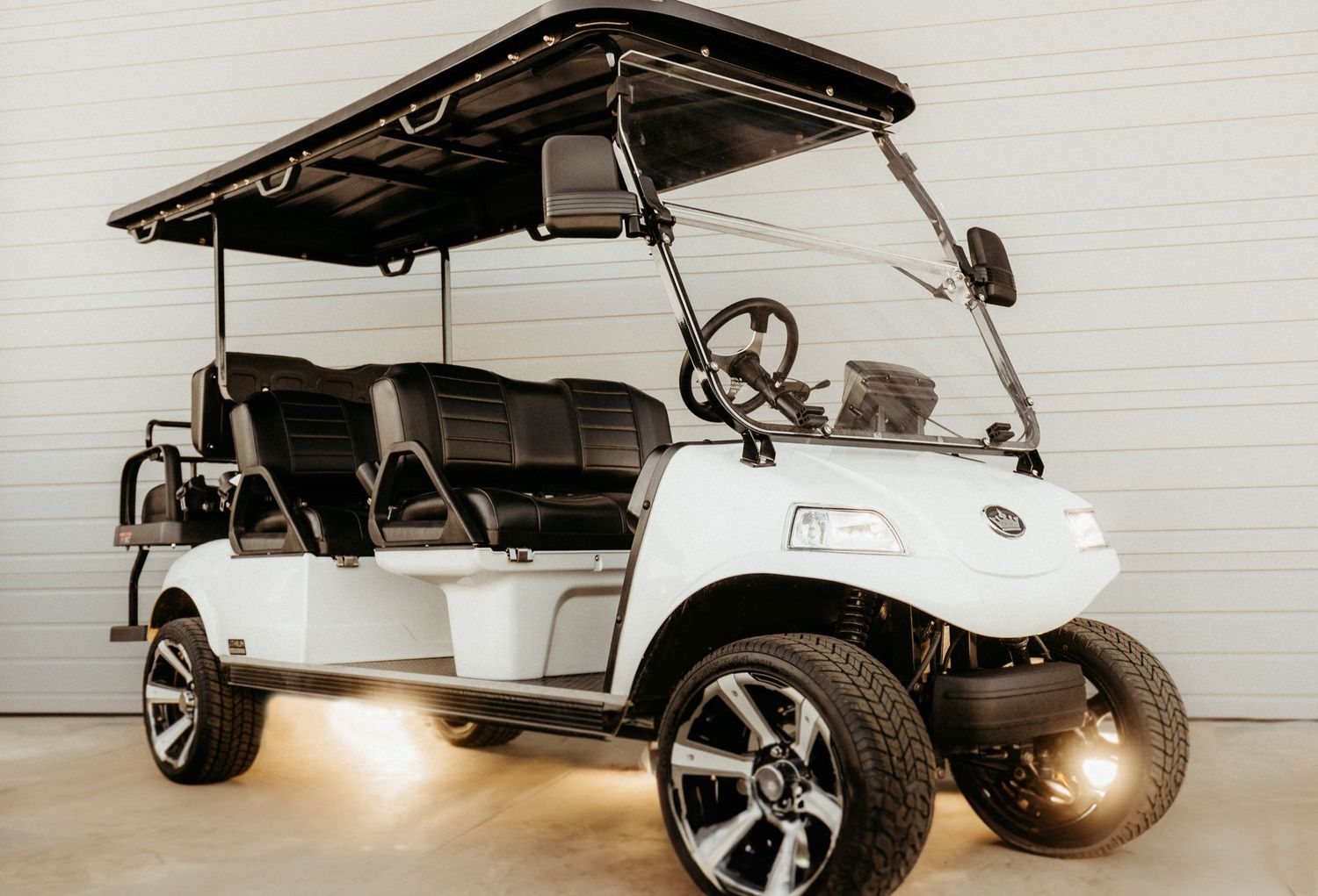 White luxury golf cart with extended seating and custom wheels parked in studio with dramatic lighting.