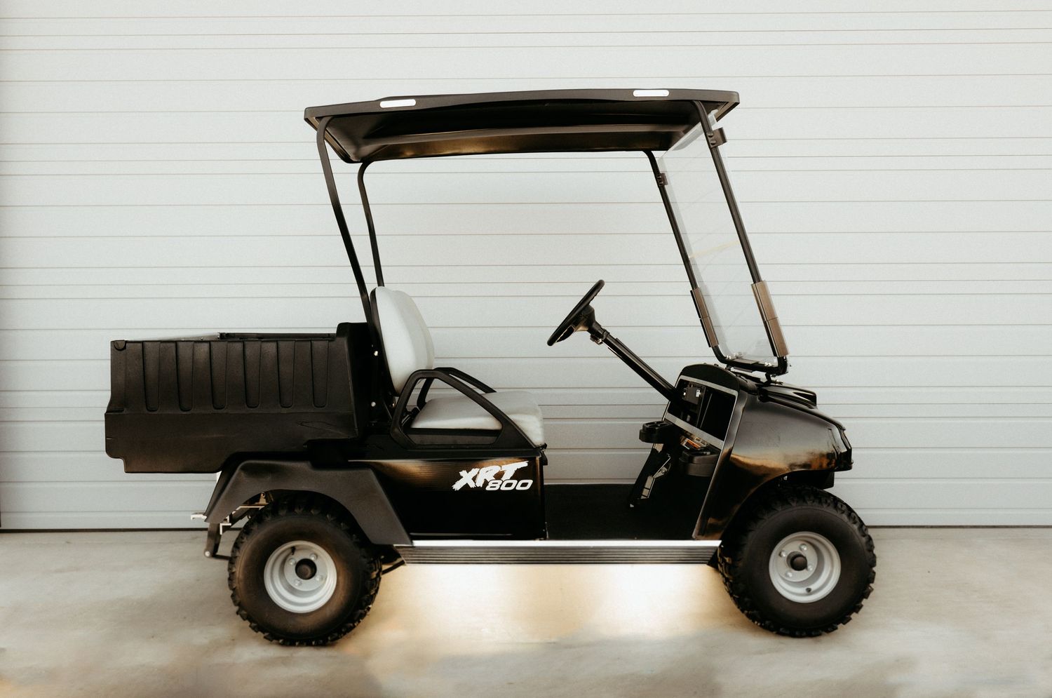 Black golf cart with utility bed parked indoors against a white garage wall.
