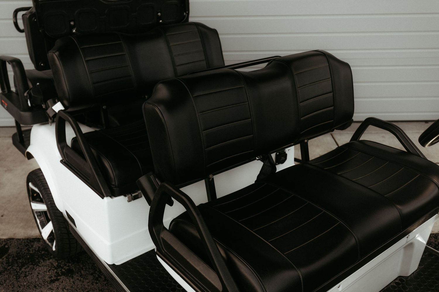 Black leather seats in custom golf cart with white exterior body and high back cushions.