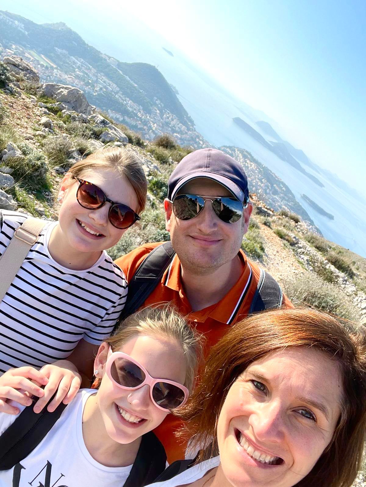 Family taking selfie together on scenic coastal mountain hiking trail.