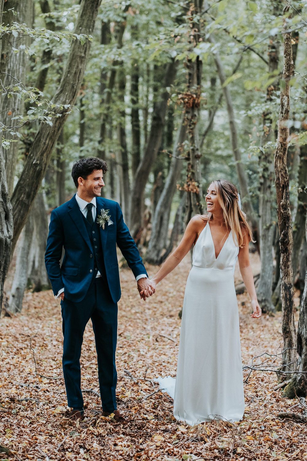 Romantic wedding couple holding hands while walking through autumn forest.