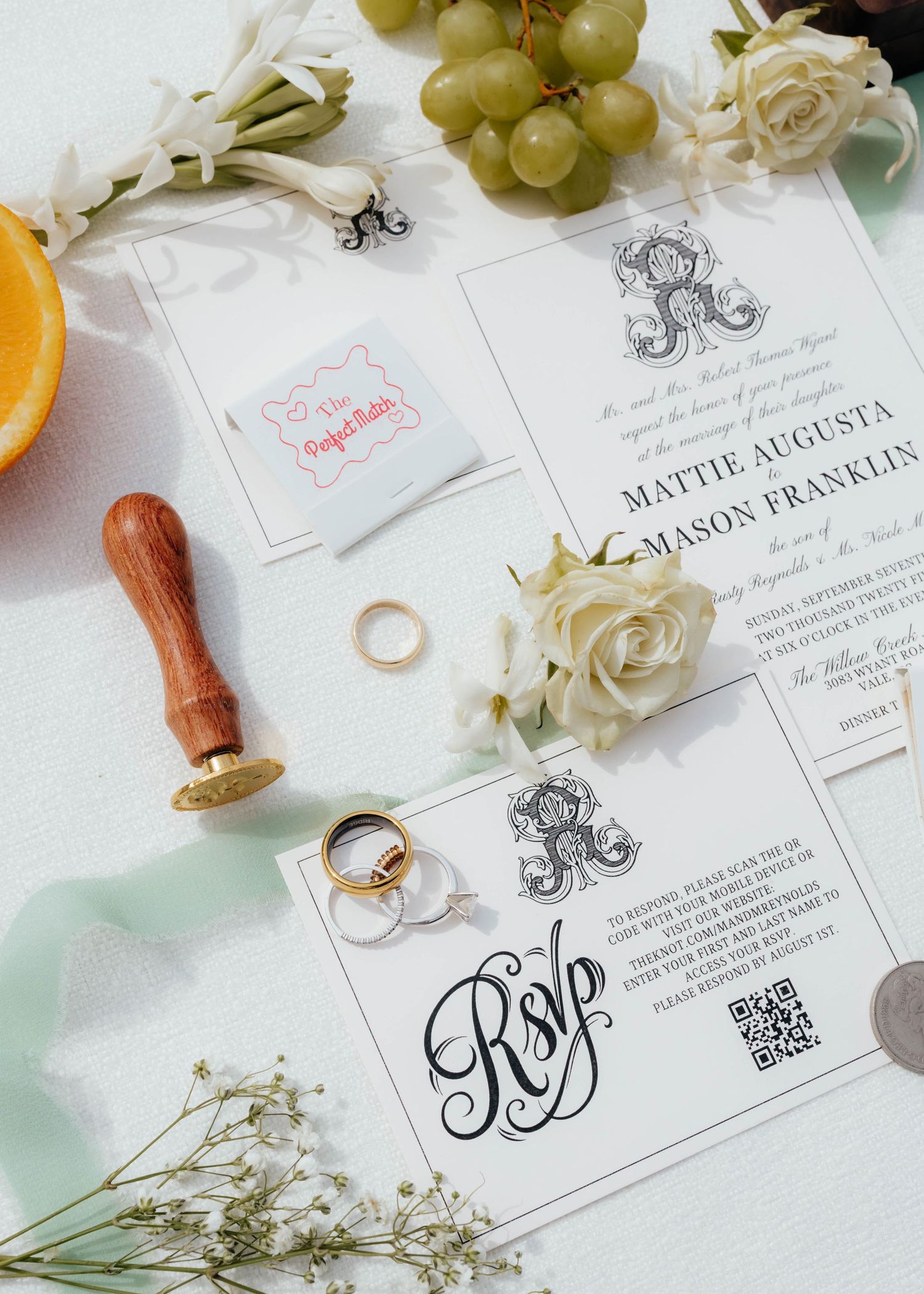 Wedding invitation suite with rings, roses, and grapes on white background.