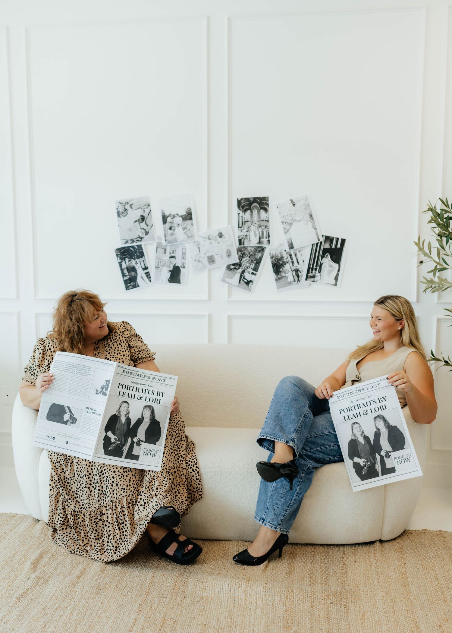 Two people sit casually on a white couch reading magazines while black and white photos decorate the wall behind them.
