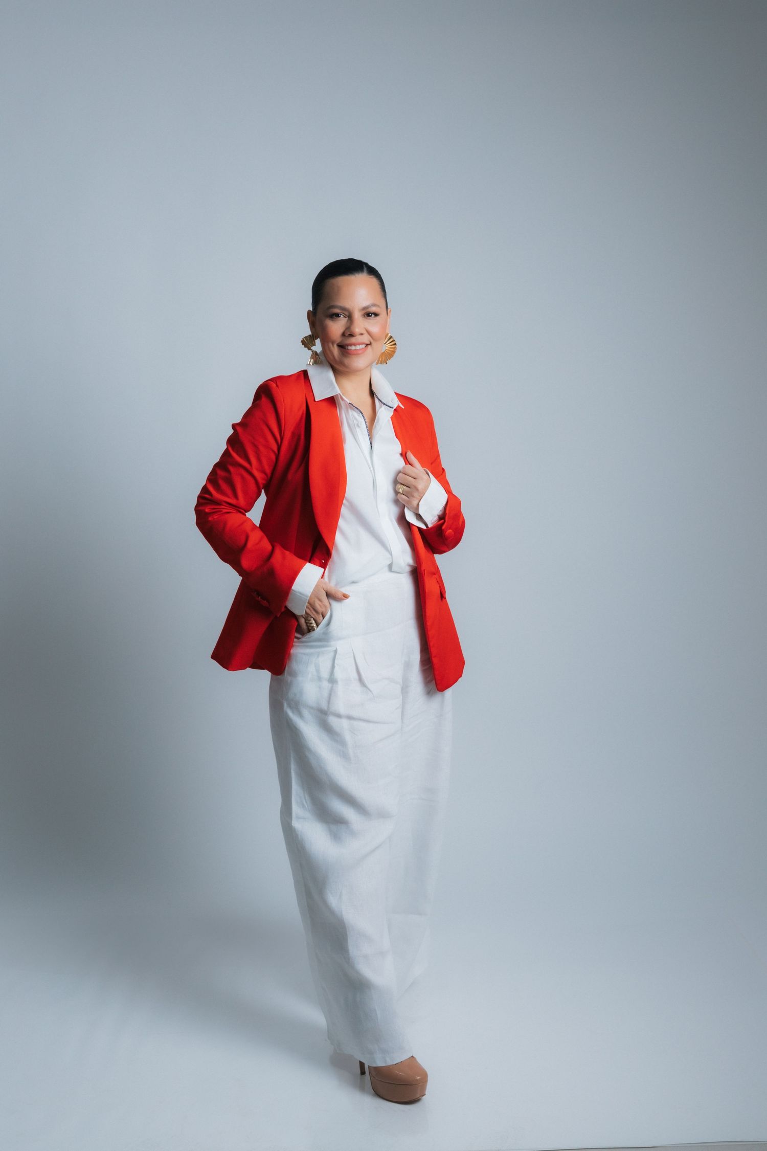 Model showcases business attire with red blazer and white ensemble in studio photoshoot.