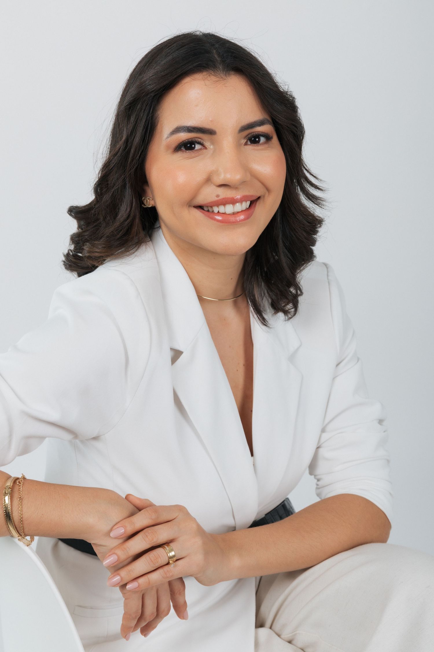 Portrait of woman in white business attire smiling warmly against neutral background.