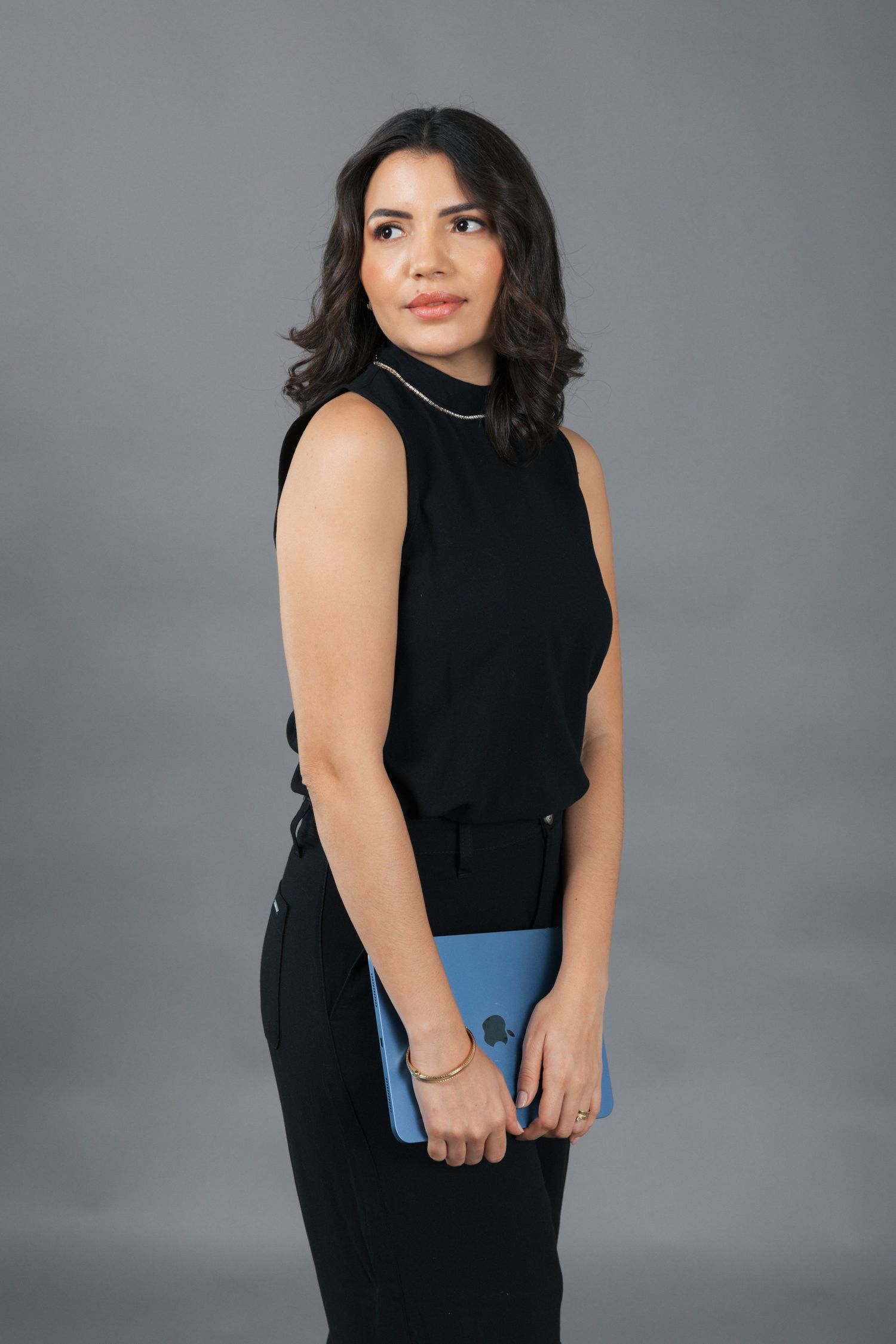 Side profile studio shot in sleeveless black top holding blue tablet against gray background.