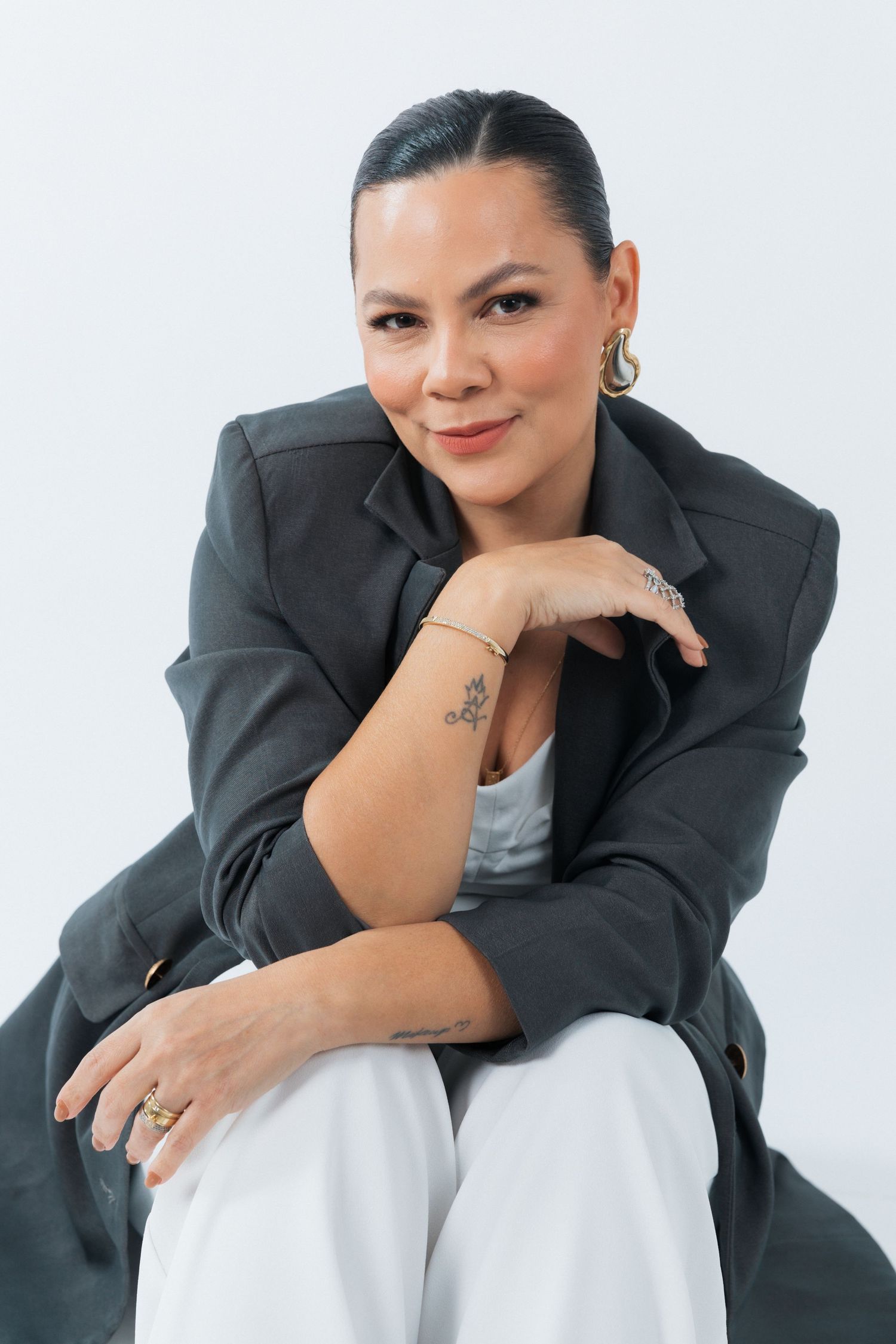 Stylish business portrait of someone in a dark blazer leaning forward with a warm expression against white backdrop.