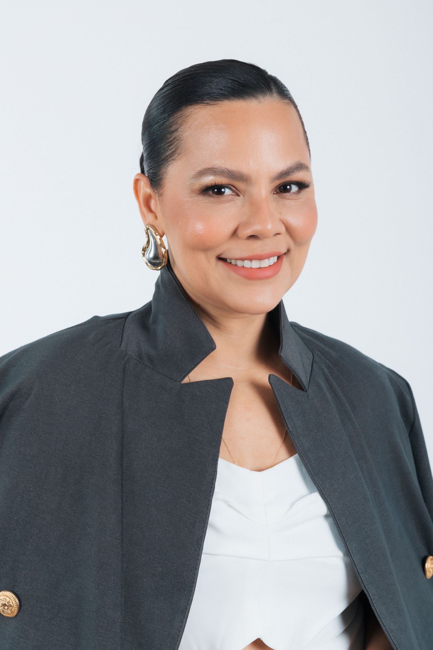 Professional headshot portrait featuring a smiling person in a dark blazer and white top against a light background.