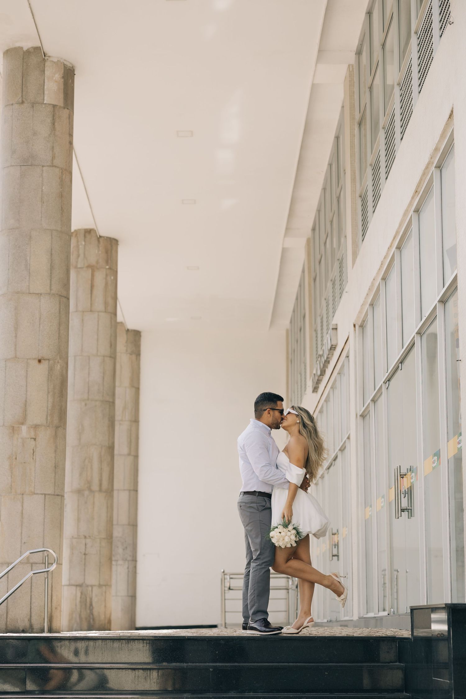 A romantic couple poses on concrete steps in front of a modern building.
