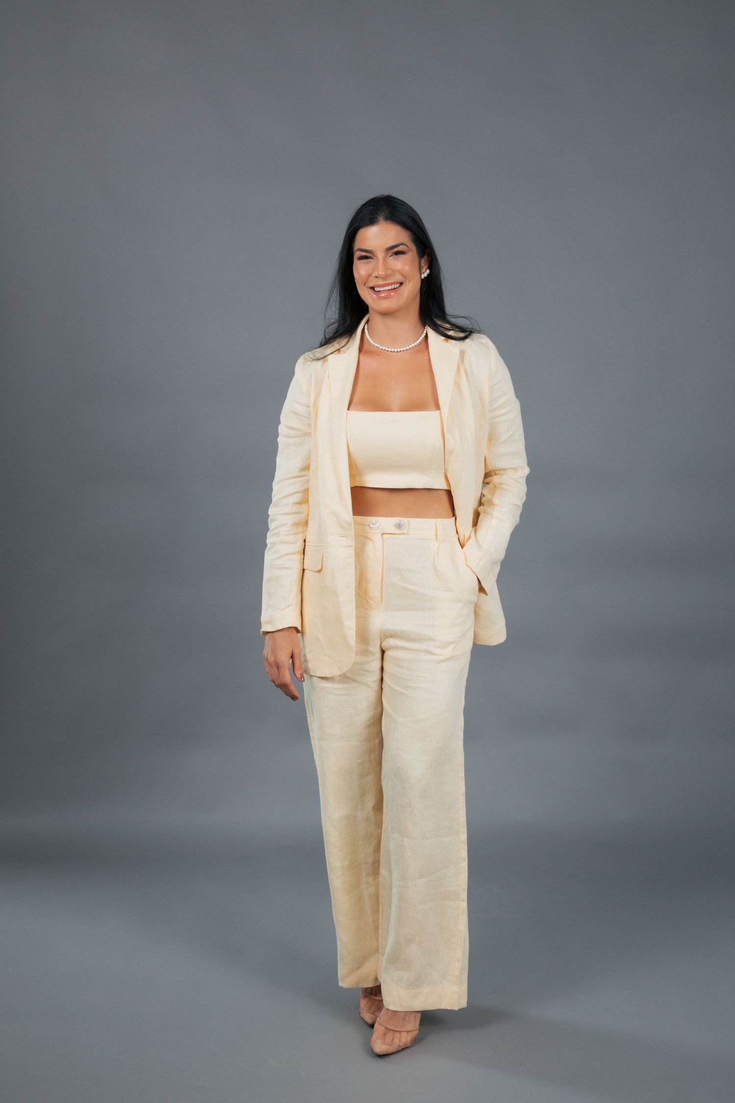 A person models a cream-colored linen pantsuit with a crop top against a gray studio backdrop.