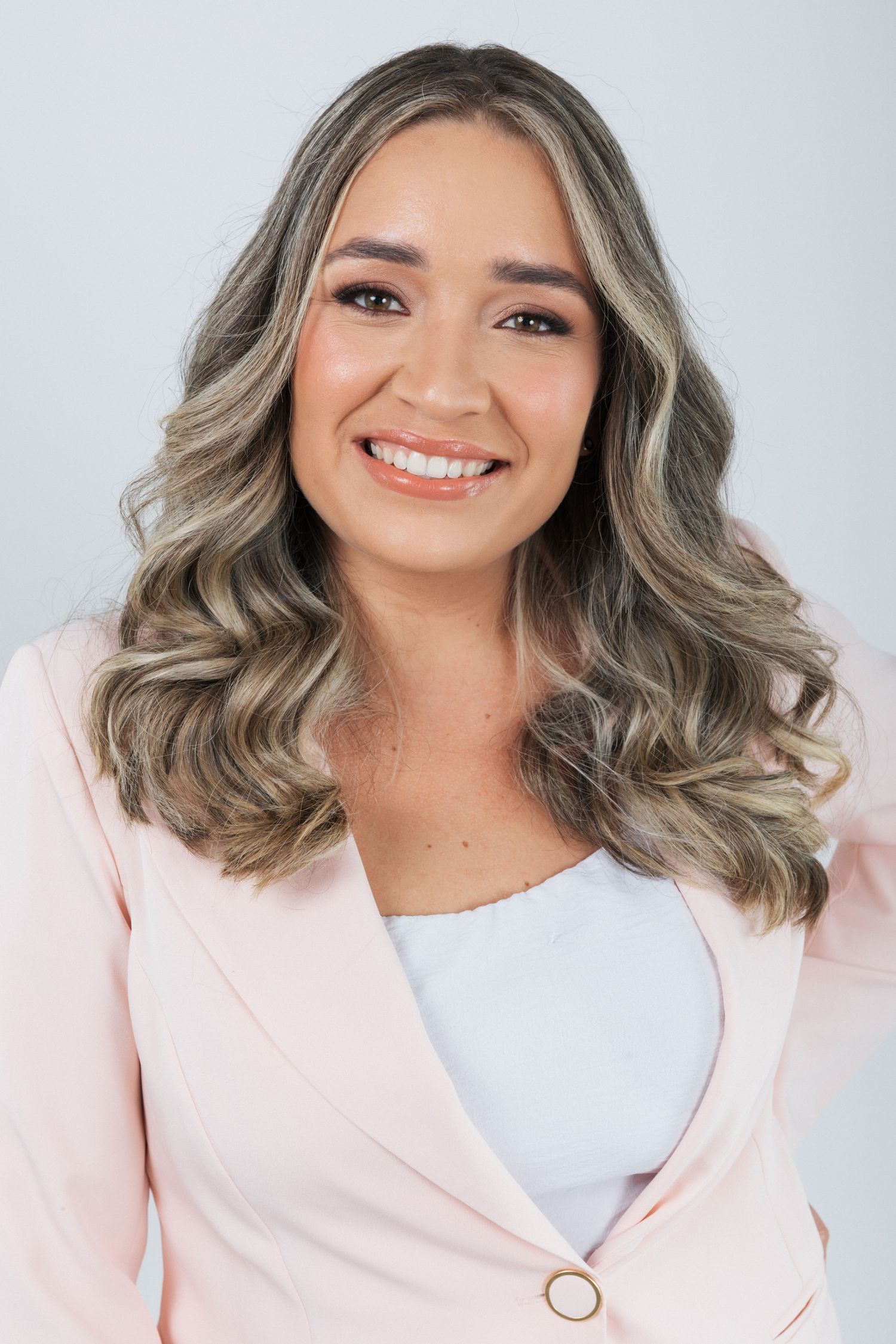 Professional portrait of someone wearing a pink blazer and white top with styled wavy gray-toned hair and a bright smile.