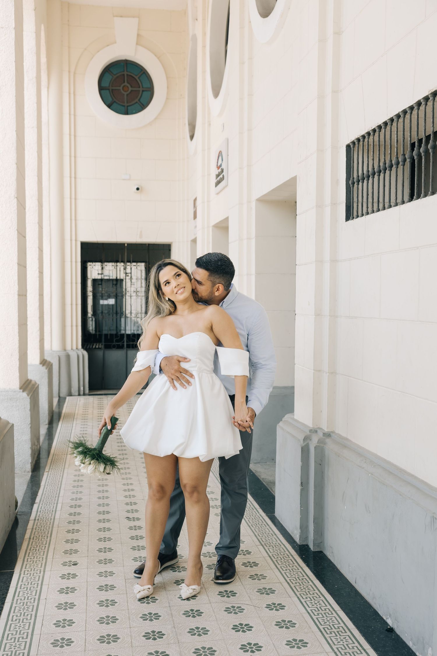 A romantic moment captured in an elegant corridor with decorative flooring and white columns.