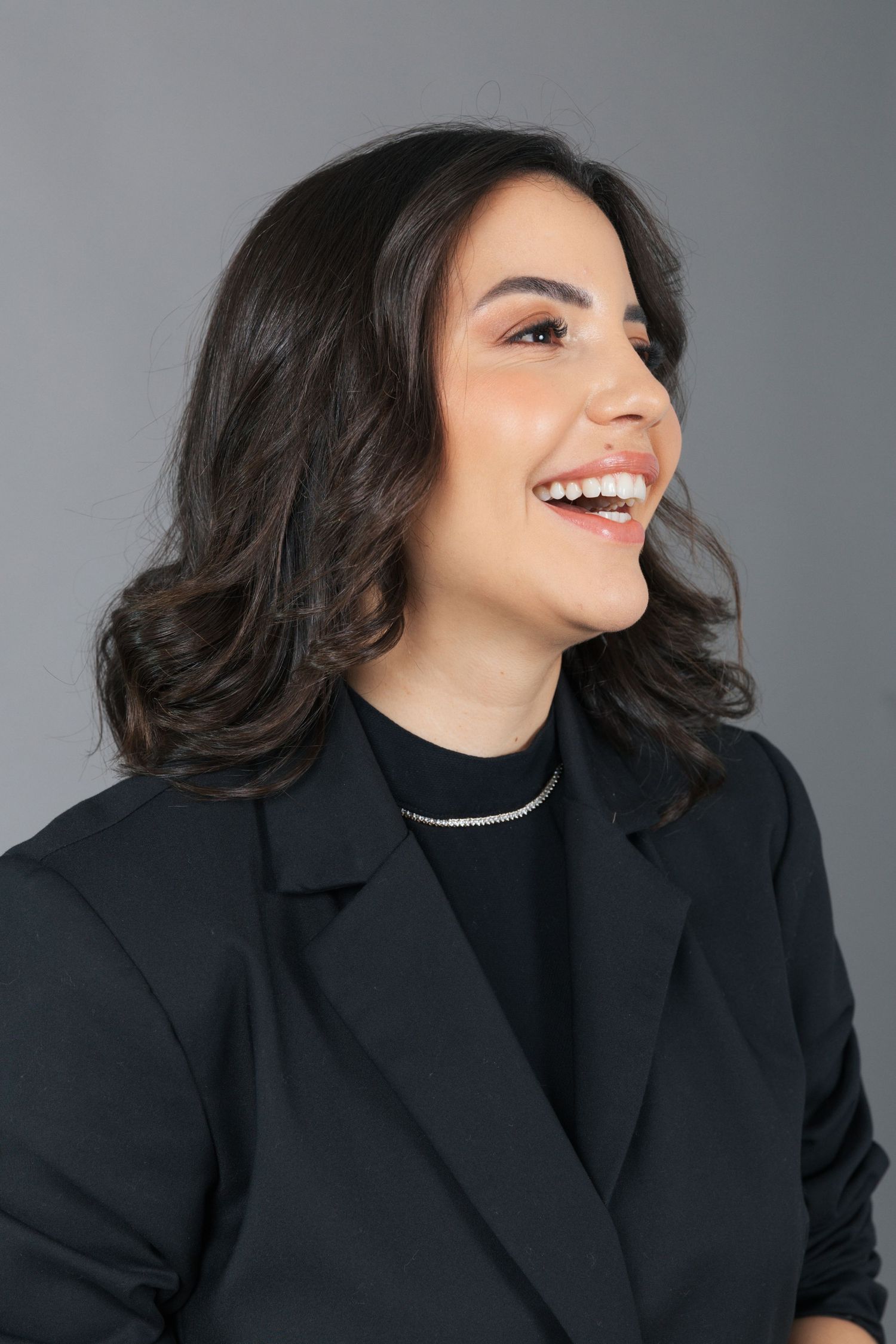 Candid portrait showing genuine laughter while wearing a black blazer and necklace.