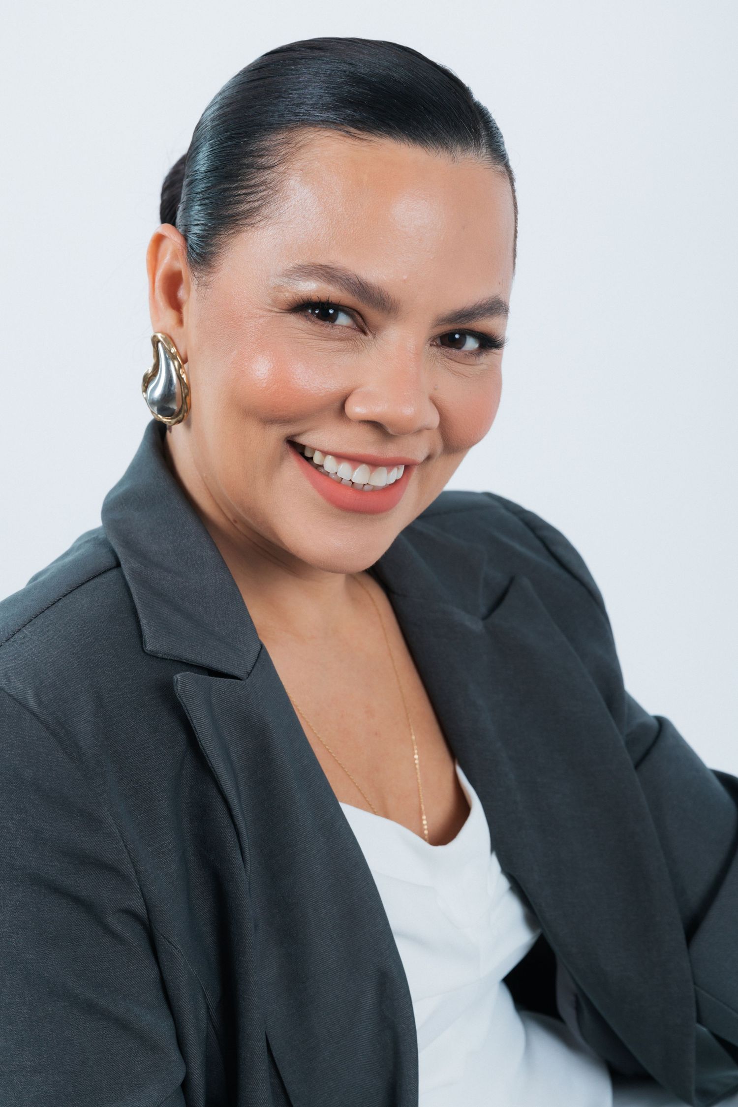 Professional headshot of someone in a dark blazer and white top smiling warmly against a light background.