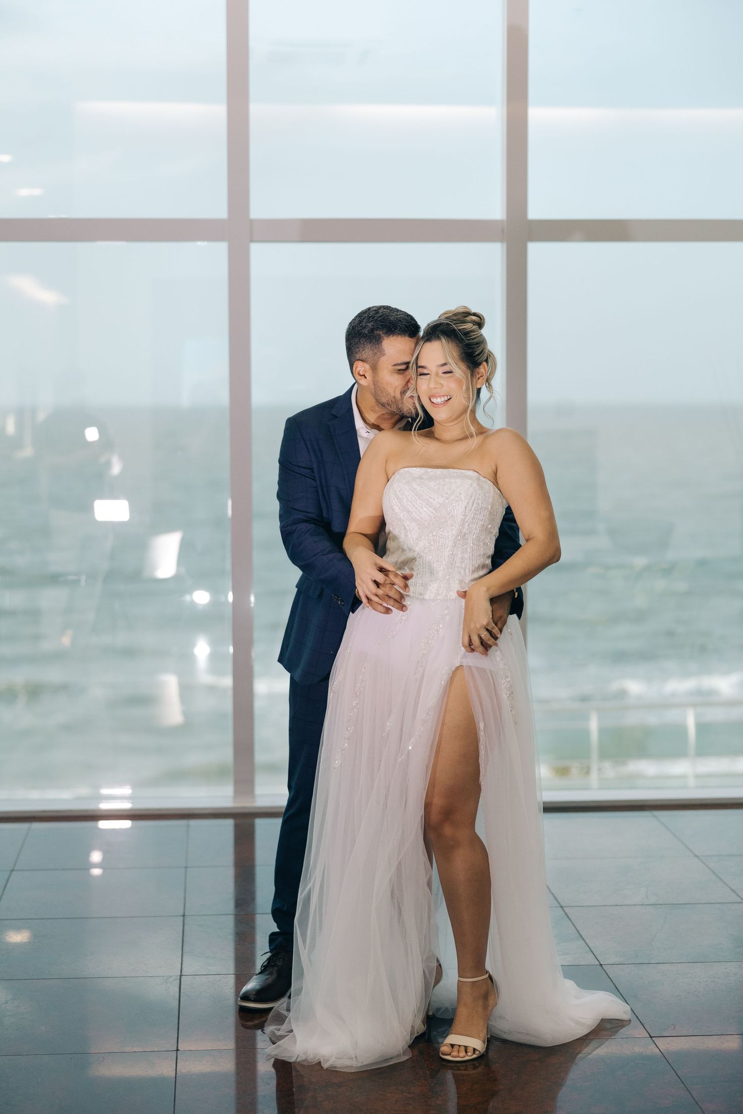 A romantic moment in formal attire against floor-to-ceiling windows overlooking a scenic view.