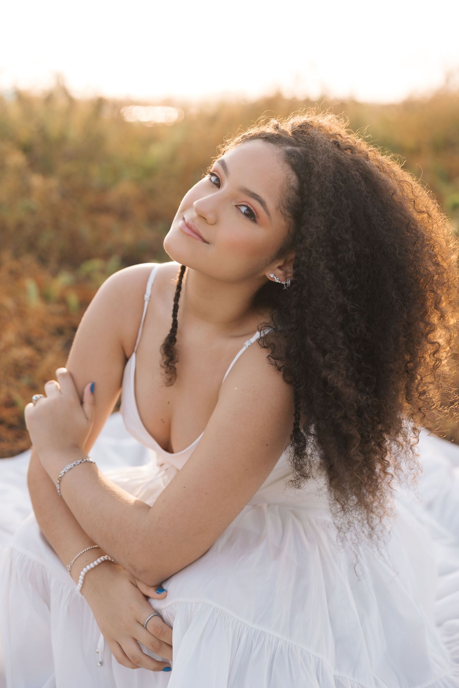 Portrait of person in flowing white dress with natural curly hair posing in golden sunset light outdoors.