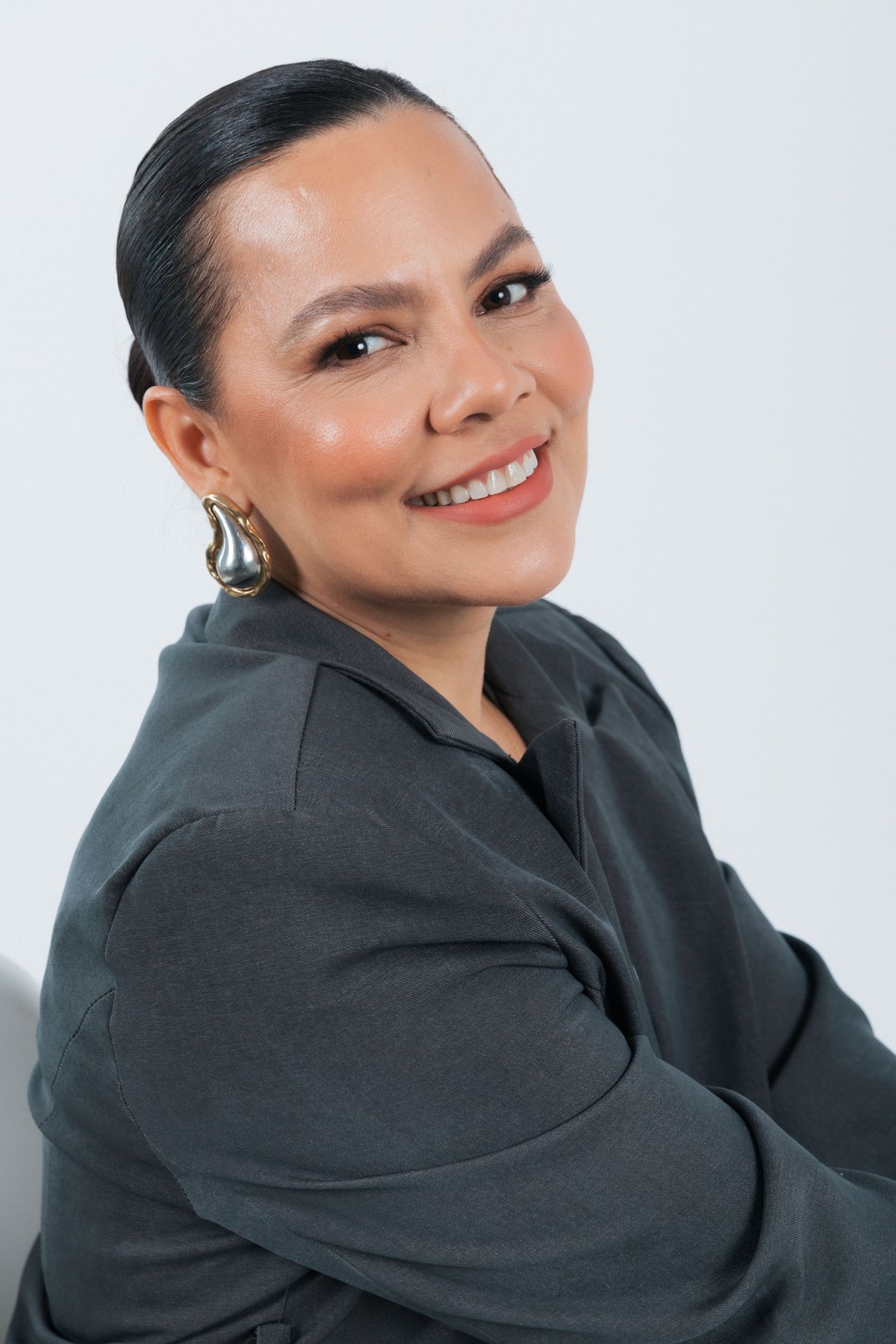 Professional headshot of someone in a dark gray sweater smiling warmly against a light background.