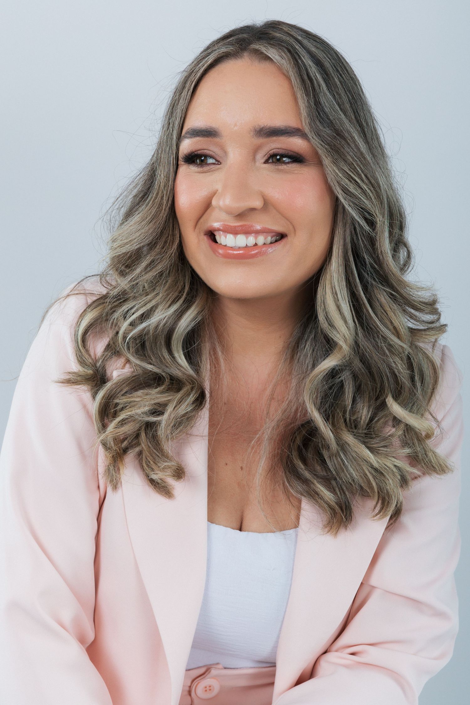 Studio headshot featuring a person in a pastel pink blazer with silver-toned wavy hair and bright smile.