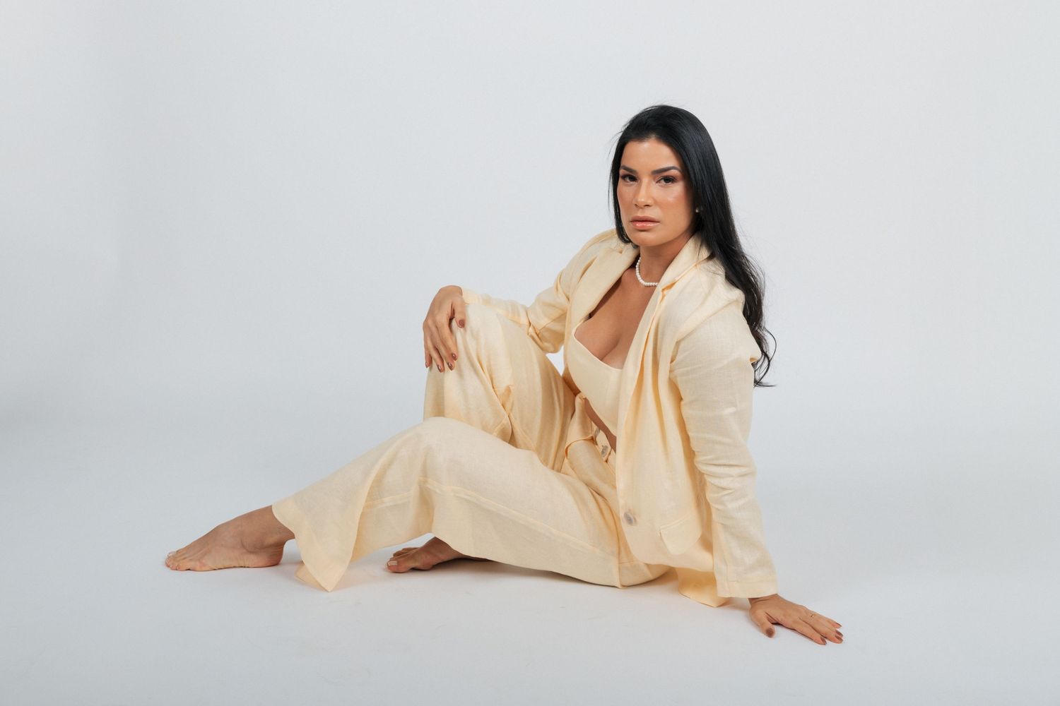 A woman in a cream colored loungewear set poses on white background.