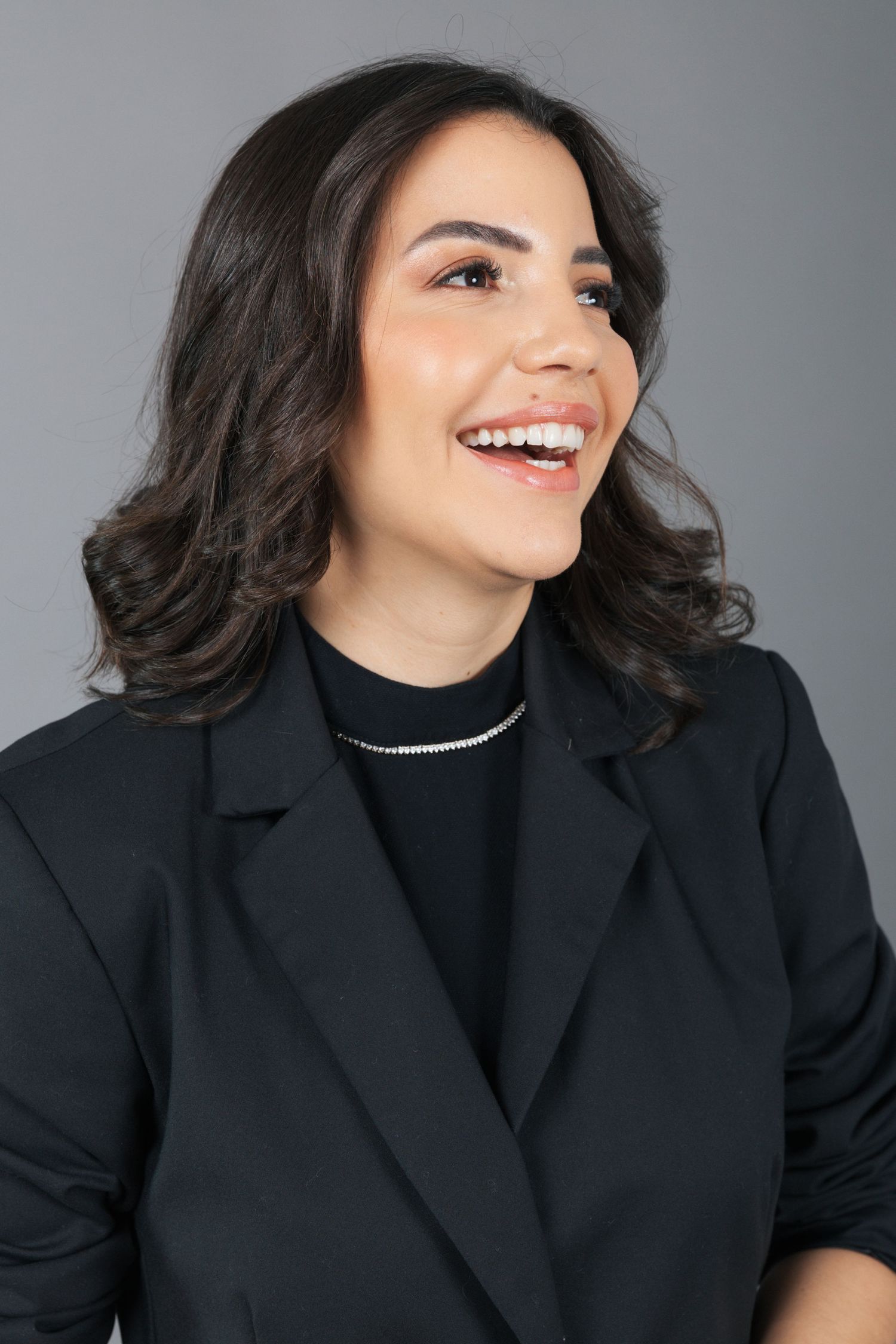 Studio portrait of a person in a black blazer laughing while looking off to the side.