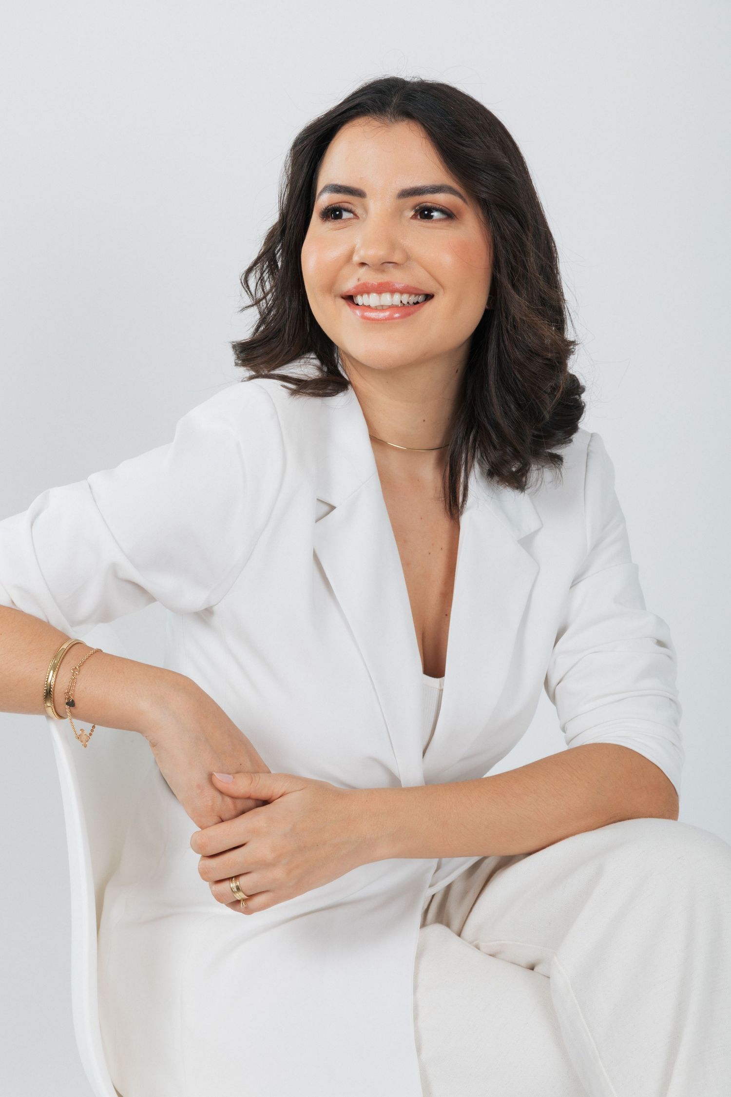 Professional headshot of someone wearing a white blazer and smiling warmly against a light background.