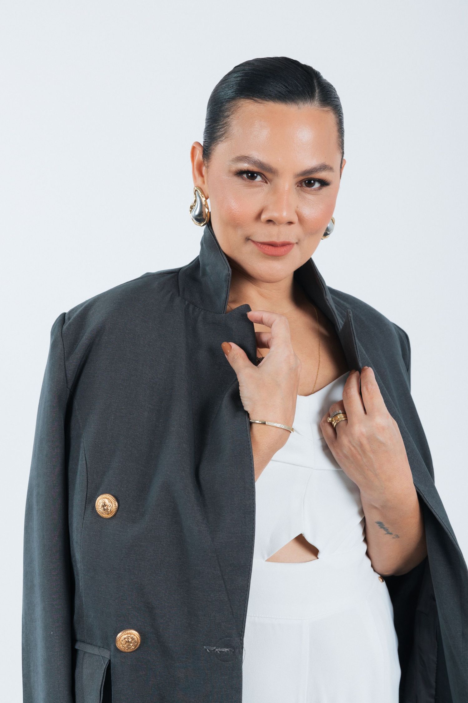 Professional studio portrait showing a sleek dark blazer with gold buttons styled over a white top against a light background.
