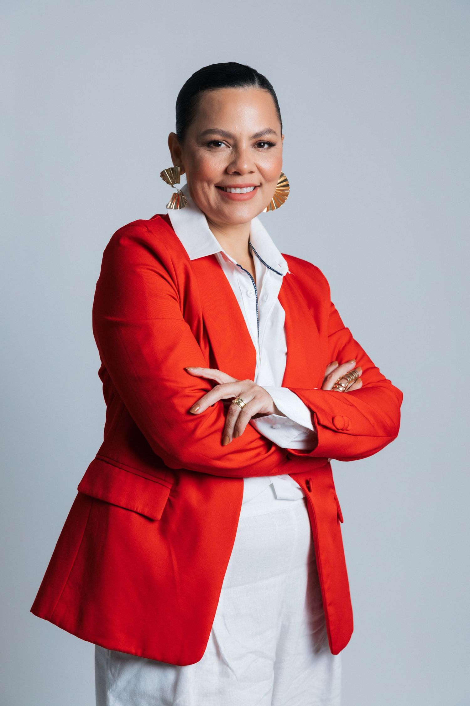 Professional studio portrait showing a bright red blazer, white outfit and metallic fan earrings.