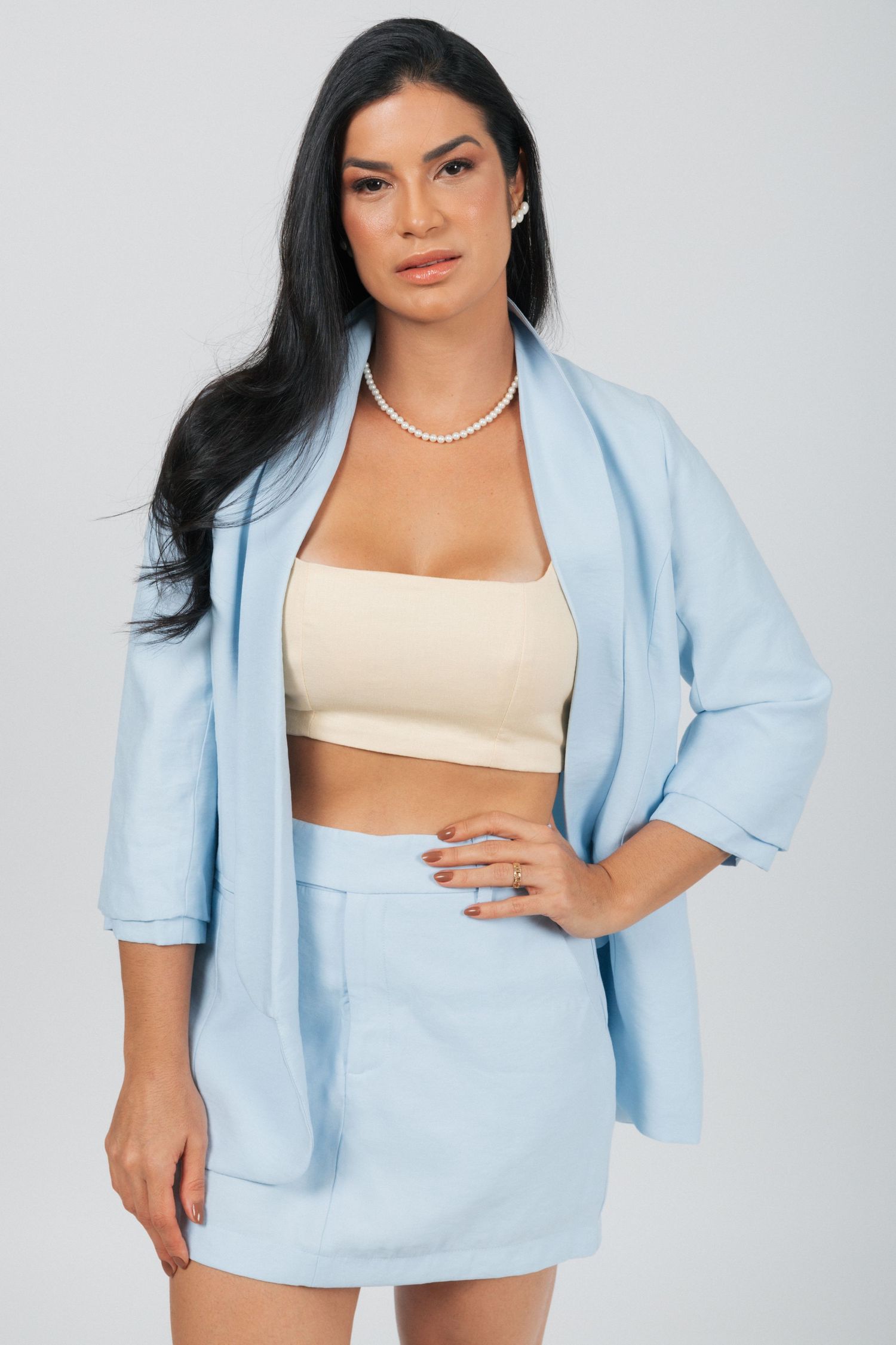 Stylish portrait showcasing light blue coordinated blazer and skirt with cream crop top and pearl accessories.