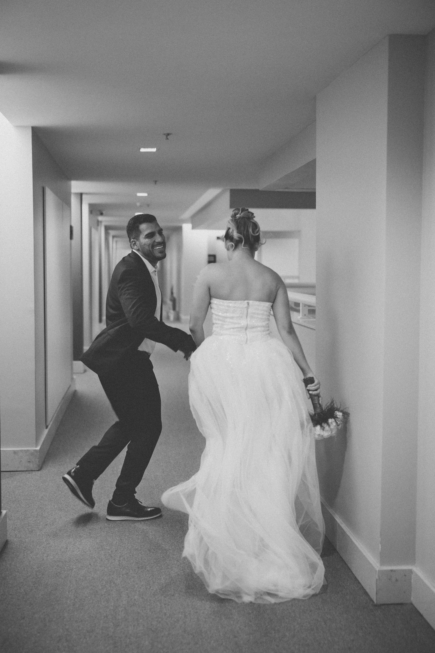 A playful black and white photo of a couple sharing a fun moment in a hotel hallway.
