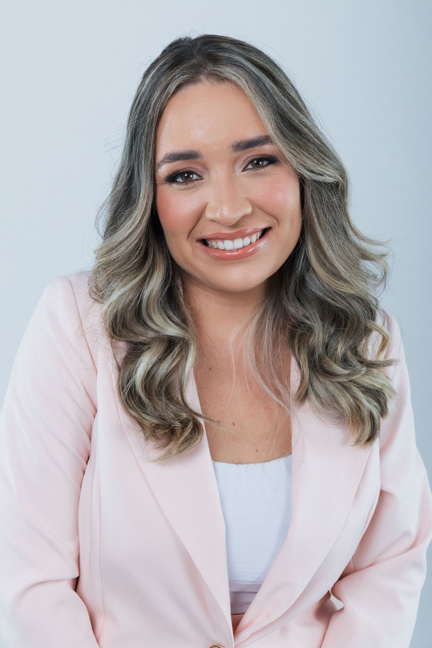 Professional portrait of someone wearing a light pink blazer and white top with stylish grey wavy hair.