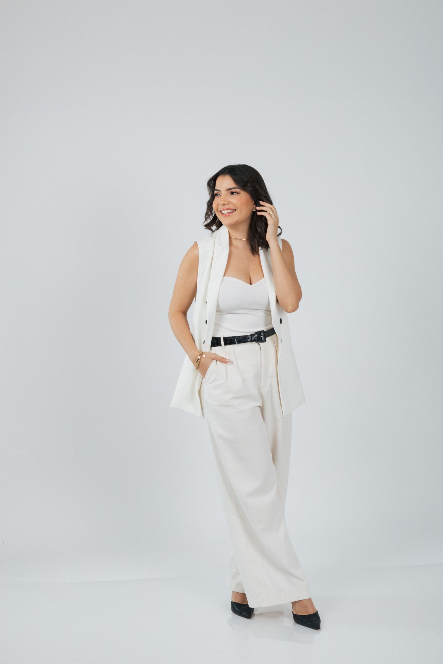 Professional woman in all-white business attire speaking on phone with hand in pocket.