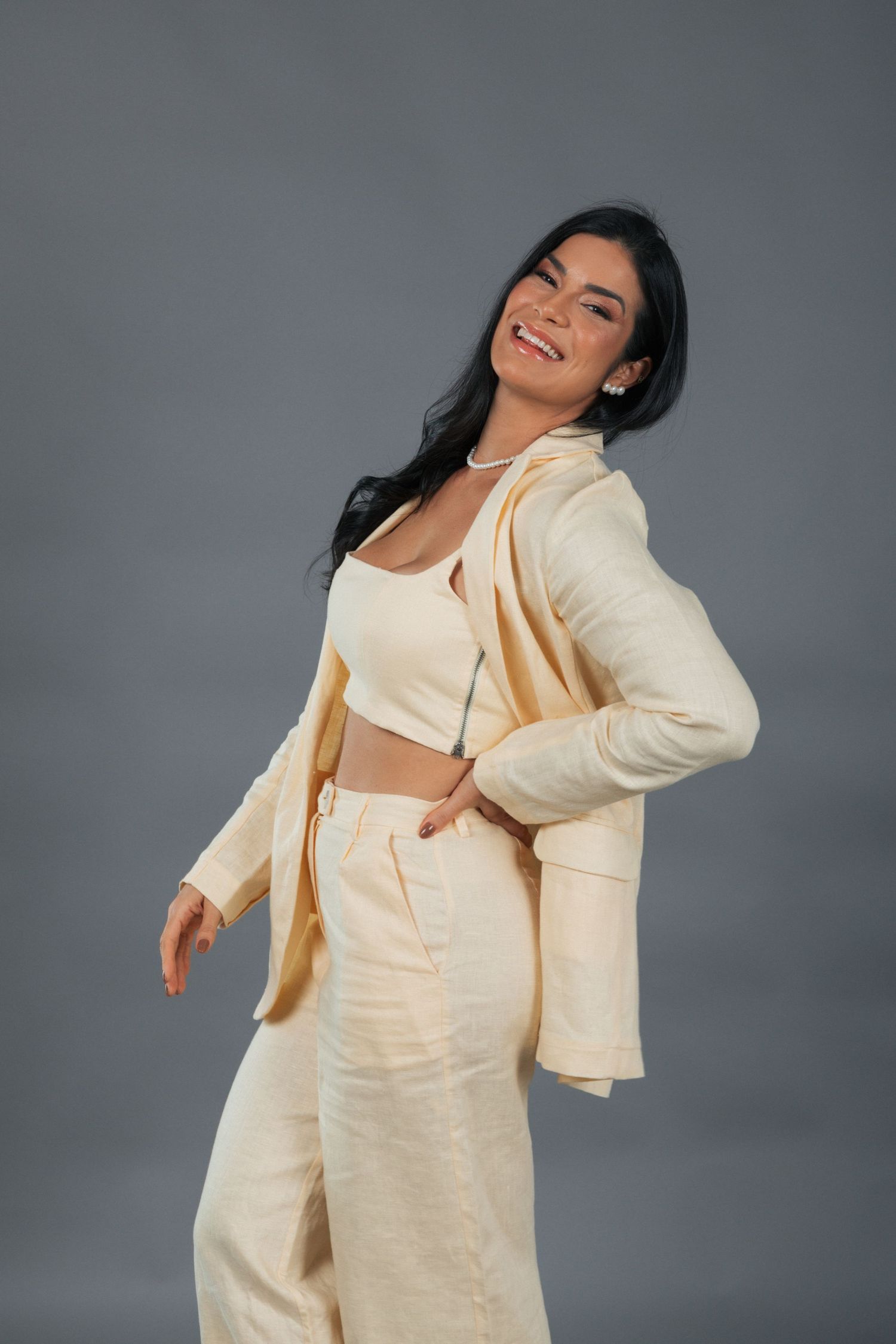 Model wearing cream colored coordinated outfit with blazer and wide leg pants posed against grey background.