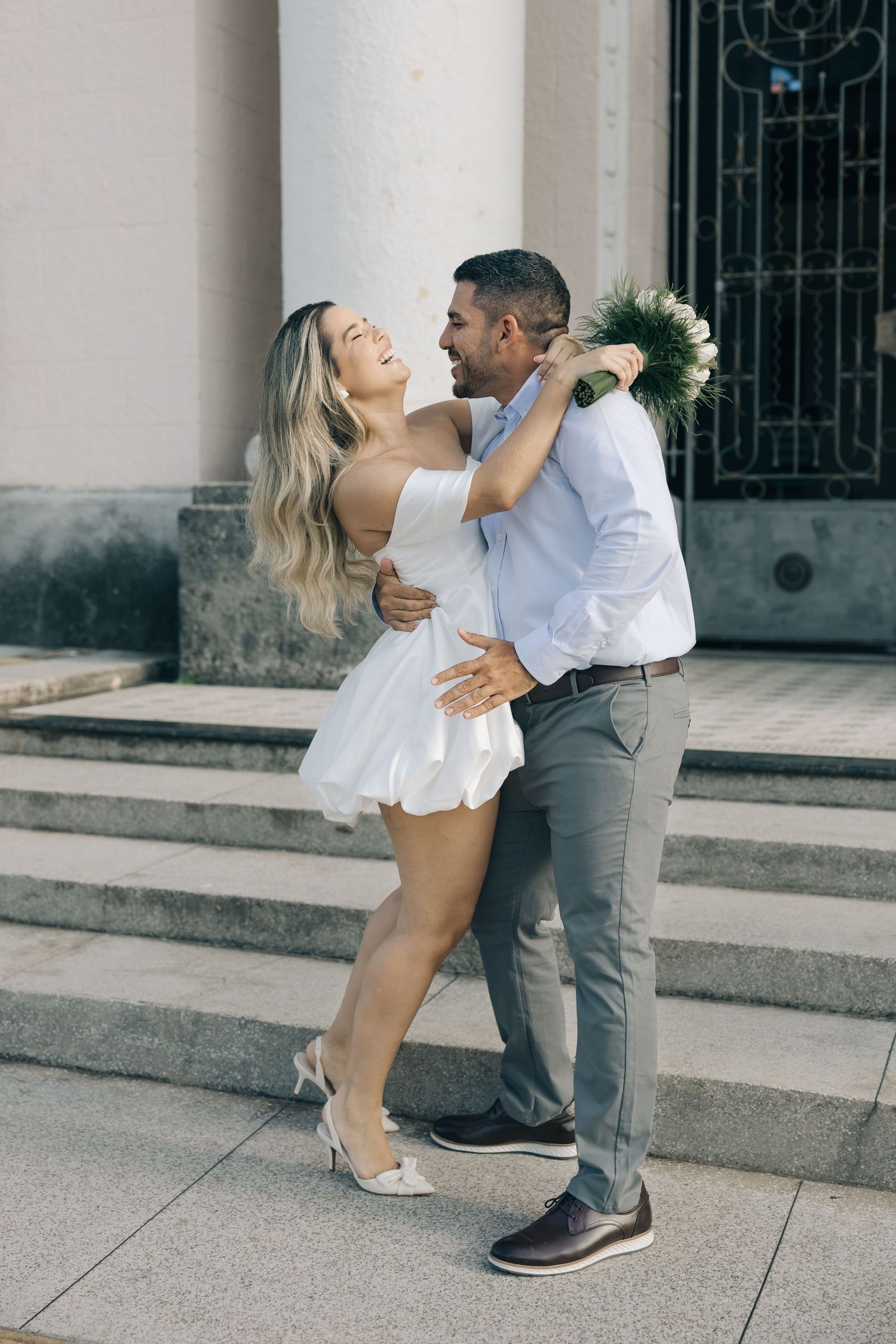 Happy engaged couple dancing and embracing on stone steps in formal attire during romantic photoshoot.