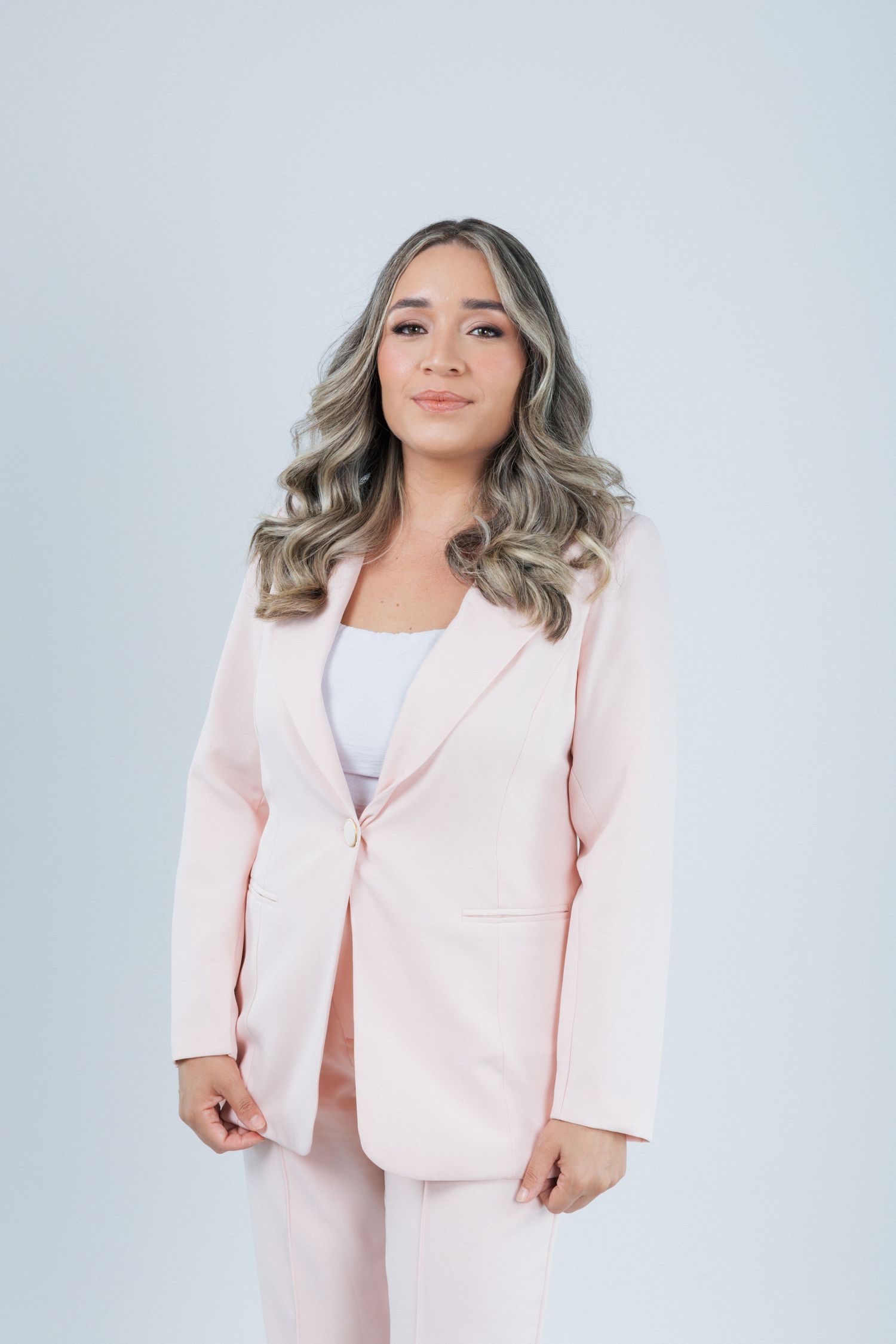 Full body business portrait showing a person in a light pink pantsuit against a plain gray backdrop.