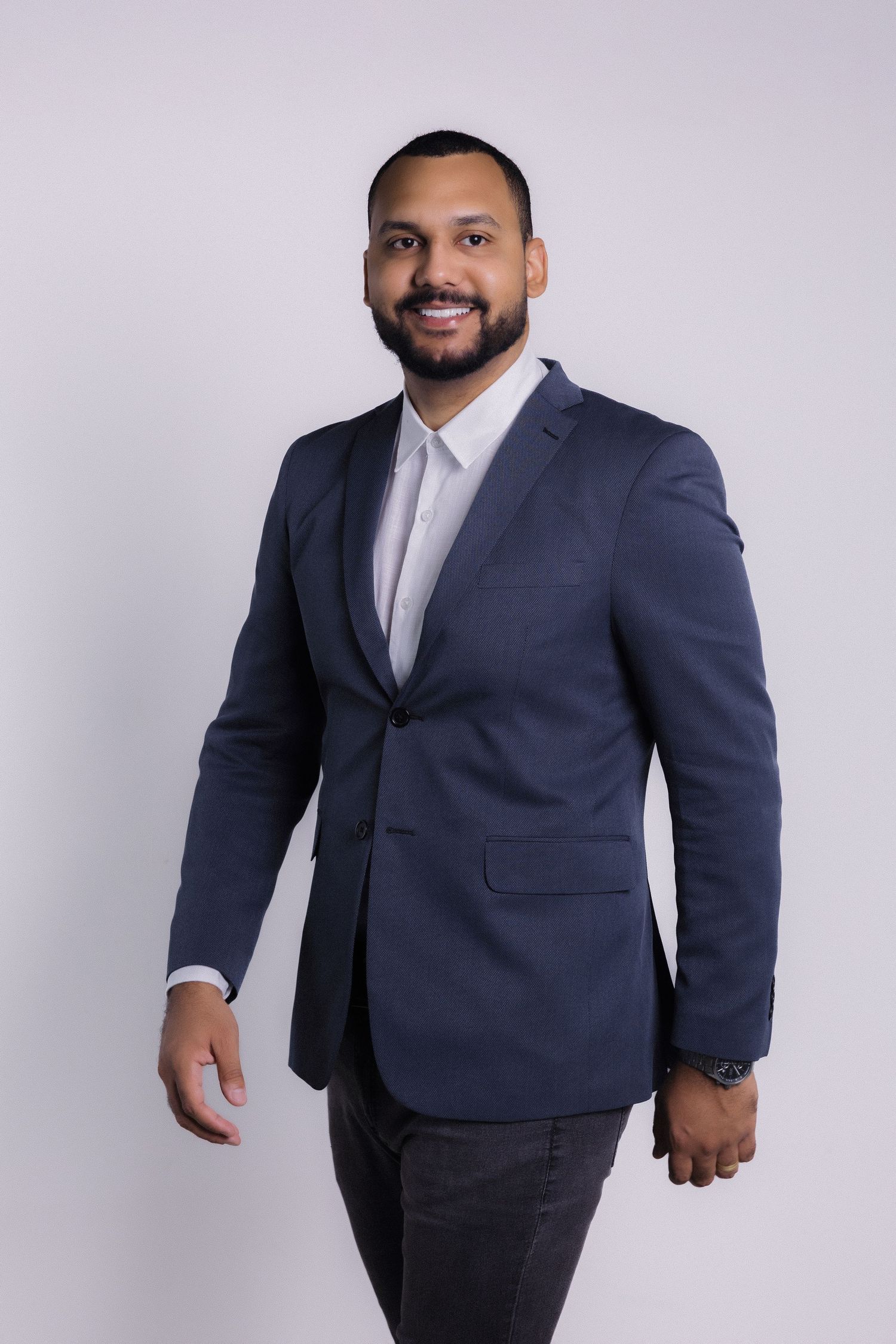 Professional headshot of someone wearing a navy blazer and white dress shirt against a light background.