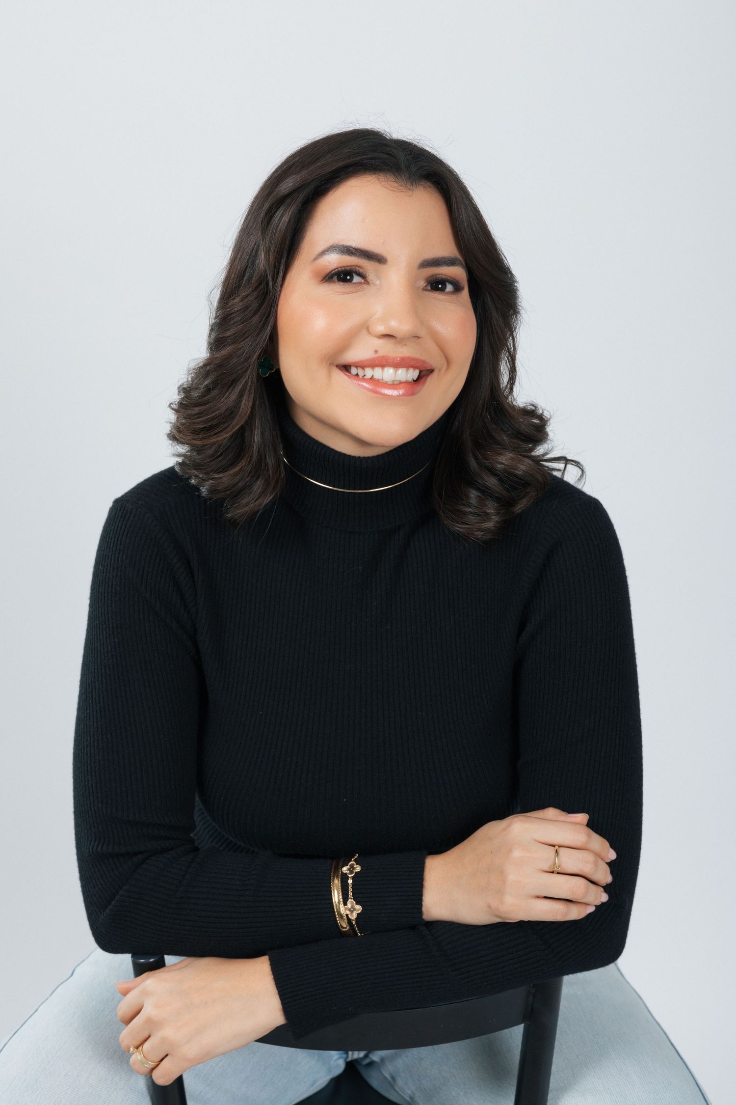 Professional portrait in black turtleneck sweater with crossed arms against light background.