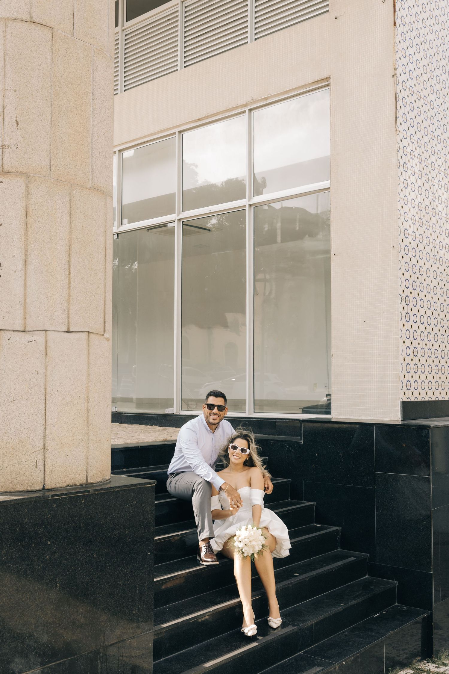A couple sits together on modern black stone steps in front of a commercial building.